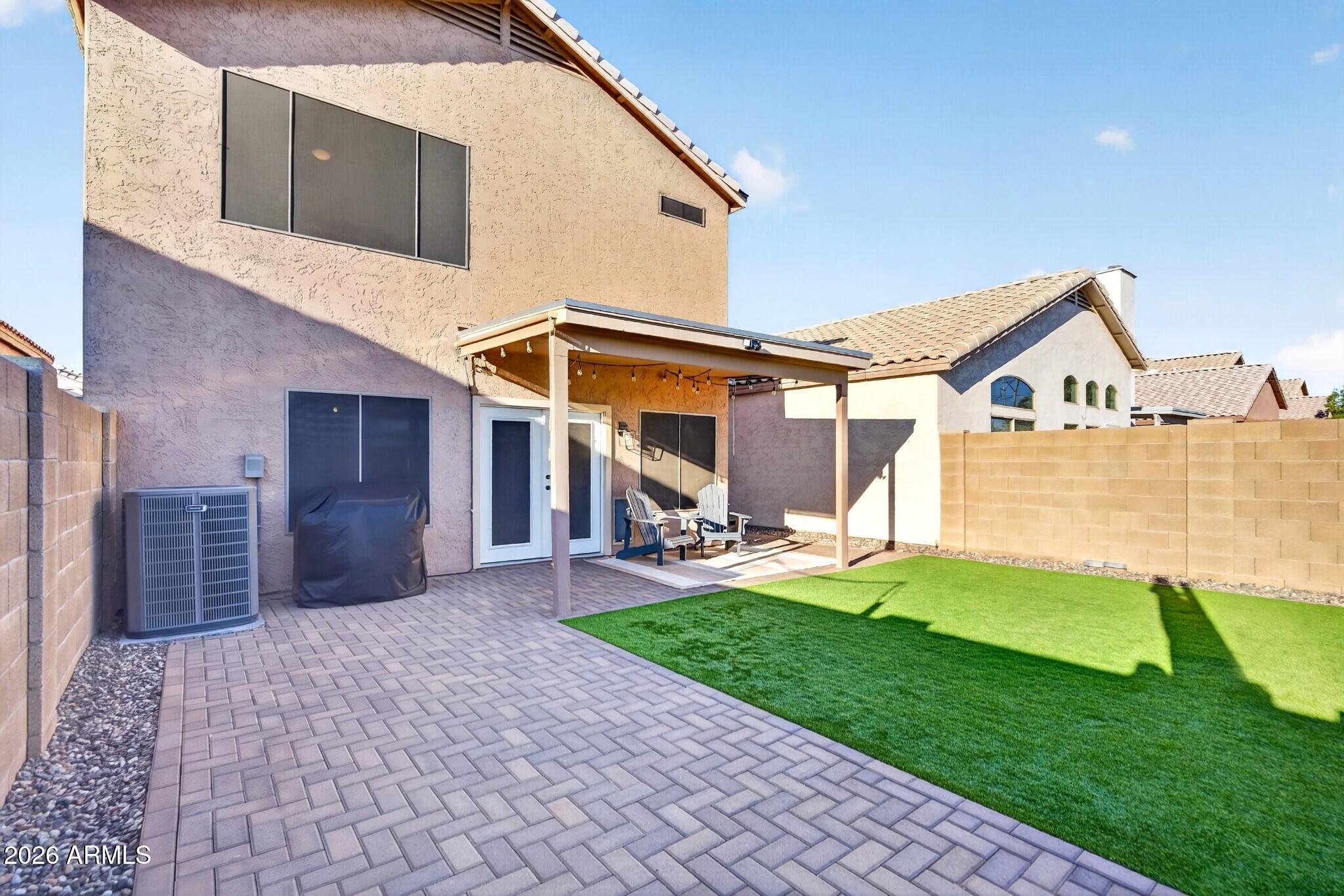 Backyard with a covered patio, outdoor seating, paver paving, and a green lawn.