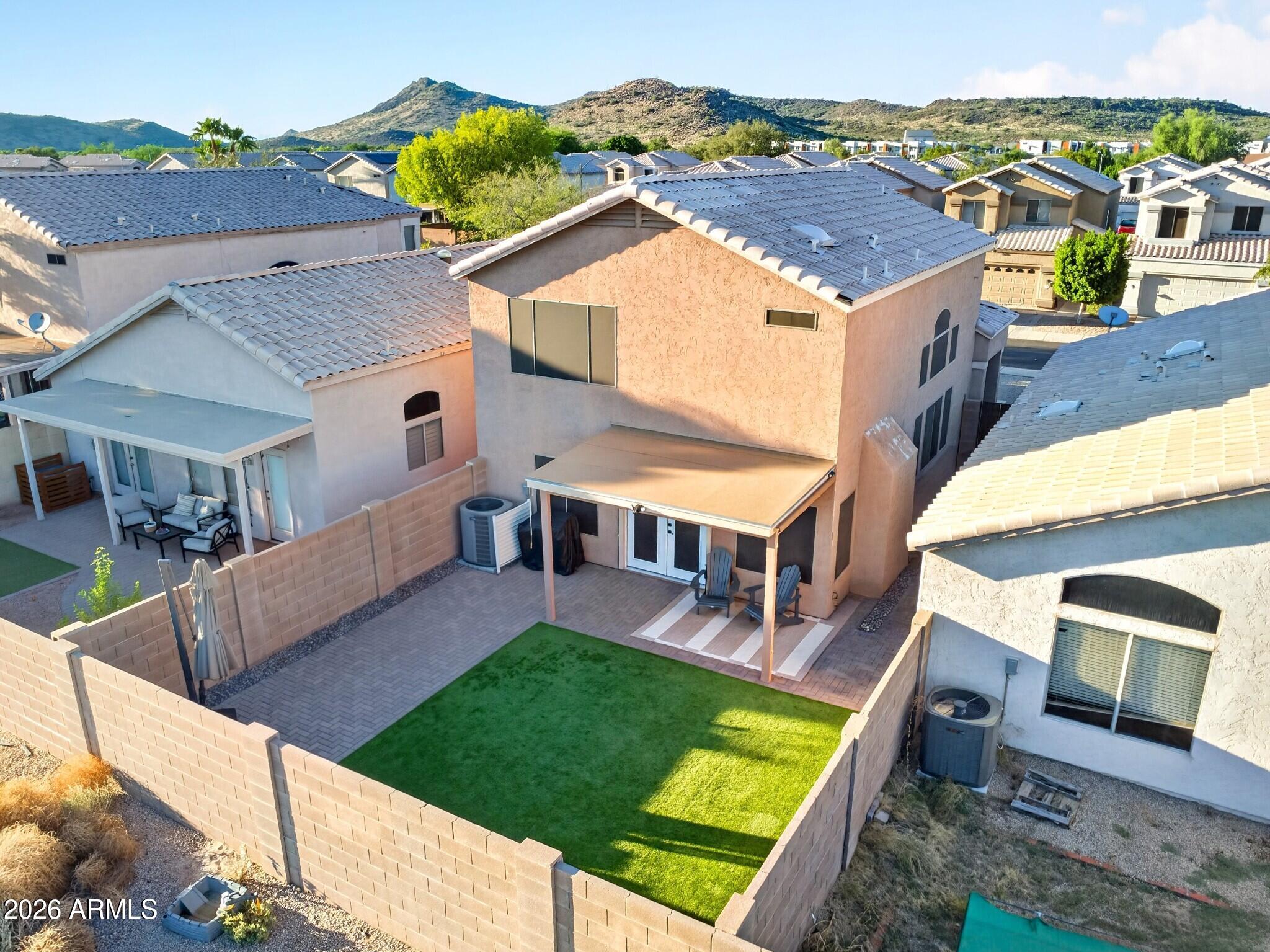 Aerial view of a two-story home with a walled lawn, covered patio, and mountains beyond.