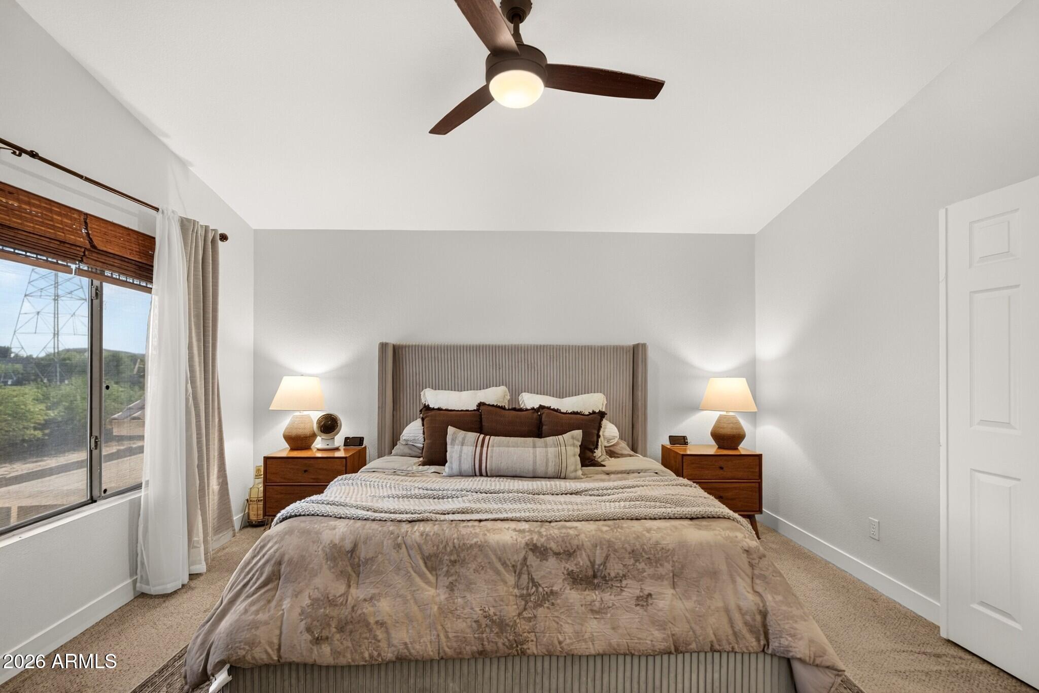 Furnished bedroom with a centered bed, matching nightstands, and a window with wooden blinds.