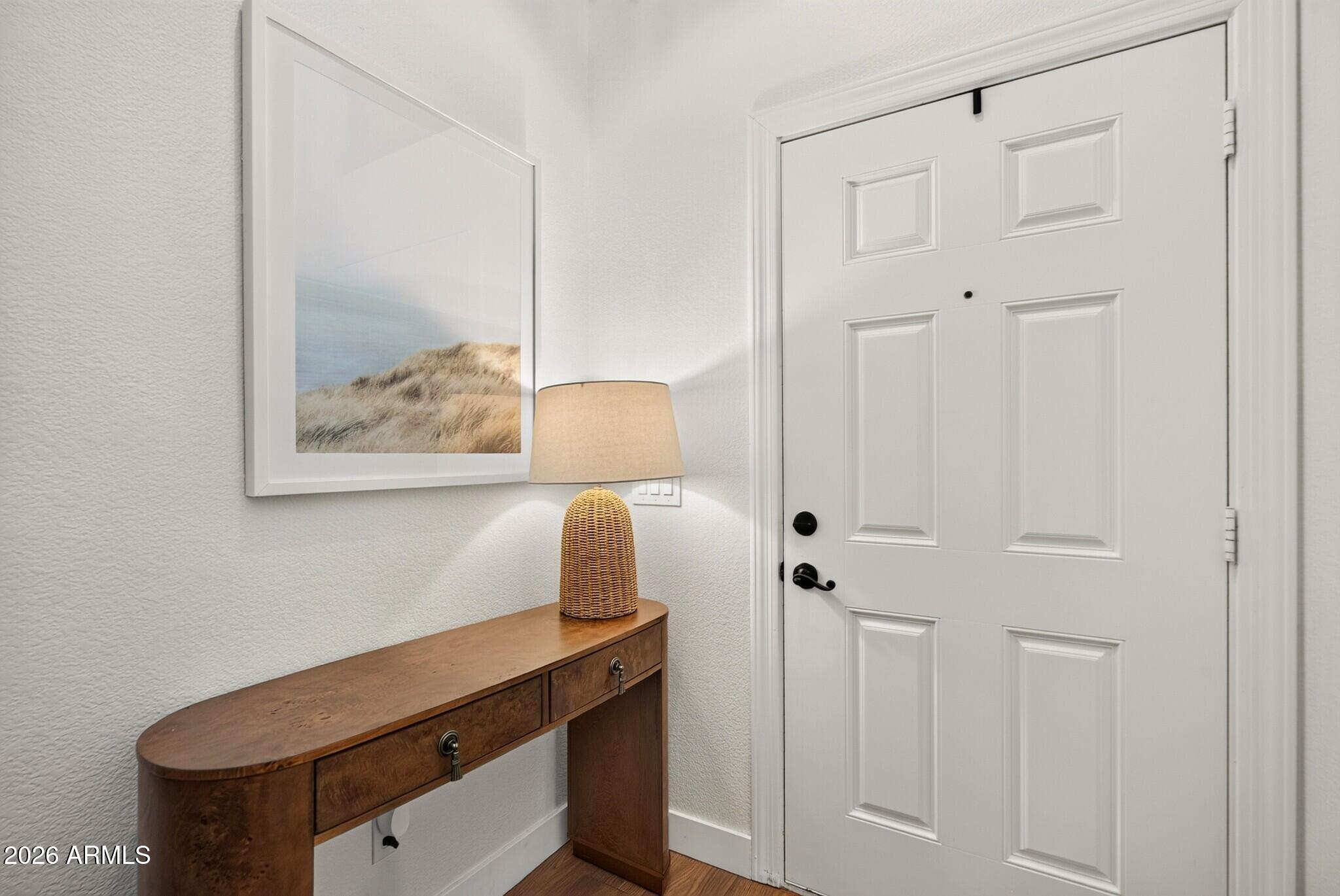 Entryway with a white paneled front door, curved wooden console table, and woven-base lamp.