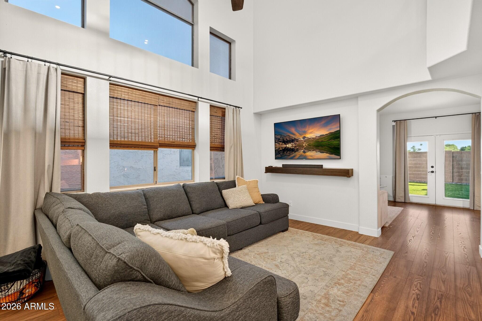 Living room with a gray sectional, tall windows, vaulted ceiling, and wood floors.