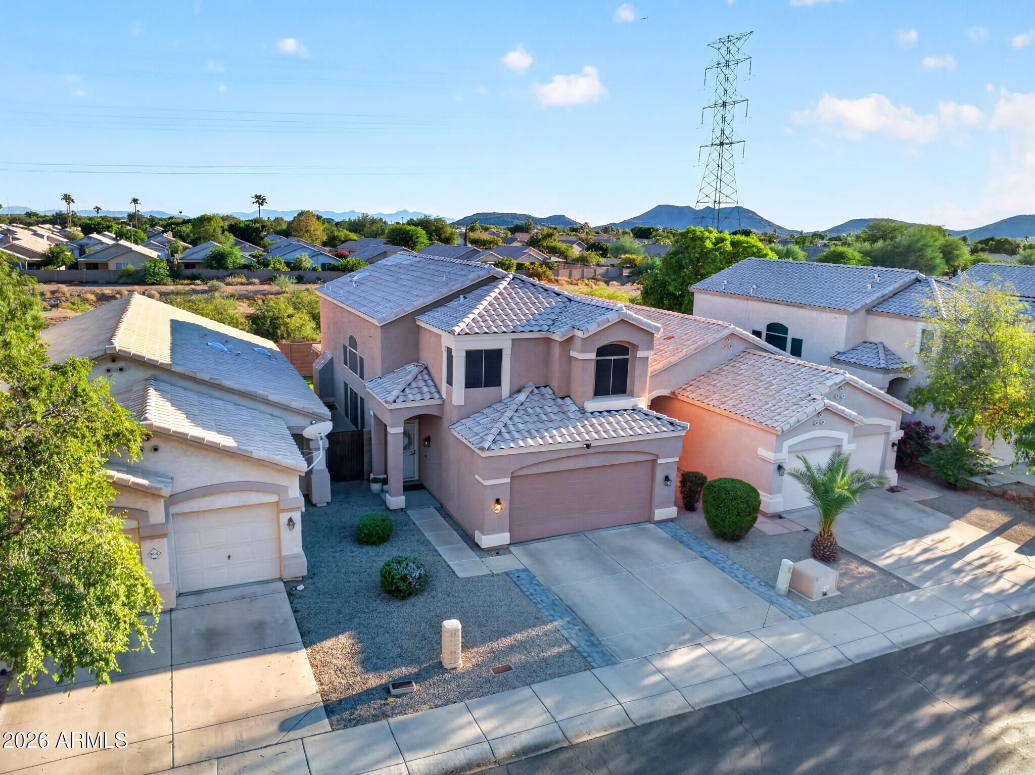 Two-story stucco home with a tiled roof and two-car garage, photographed from above with mountains behind it.