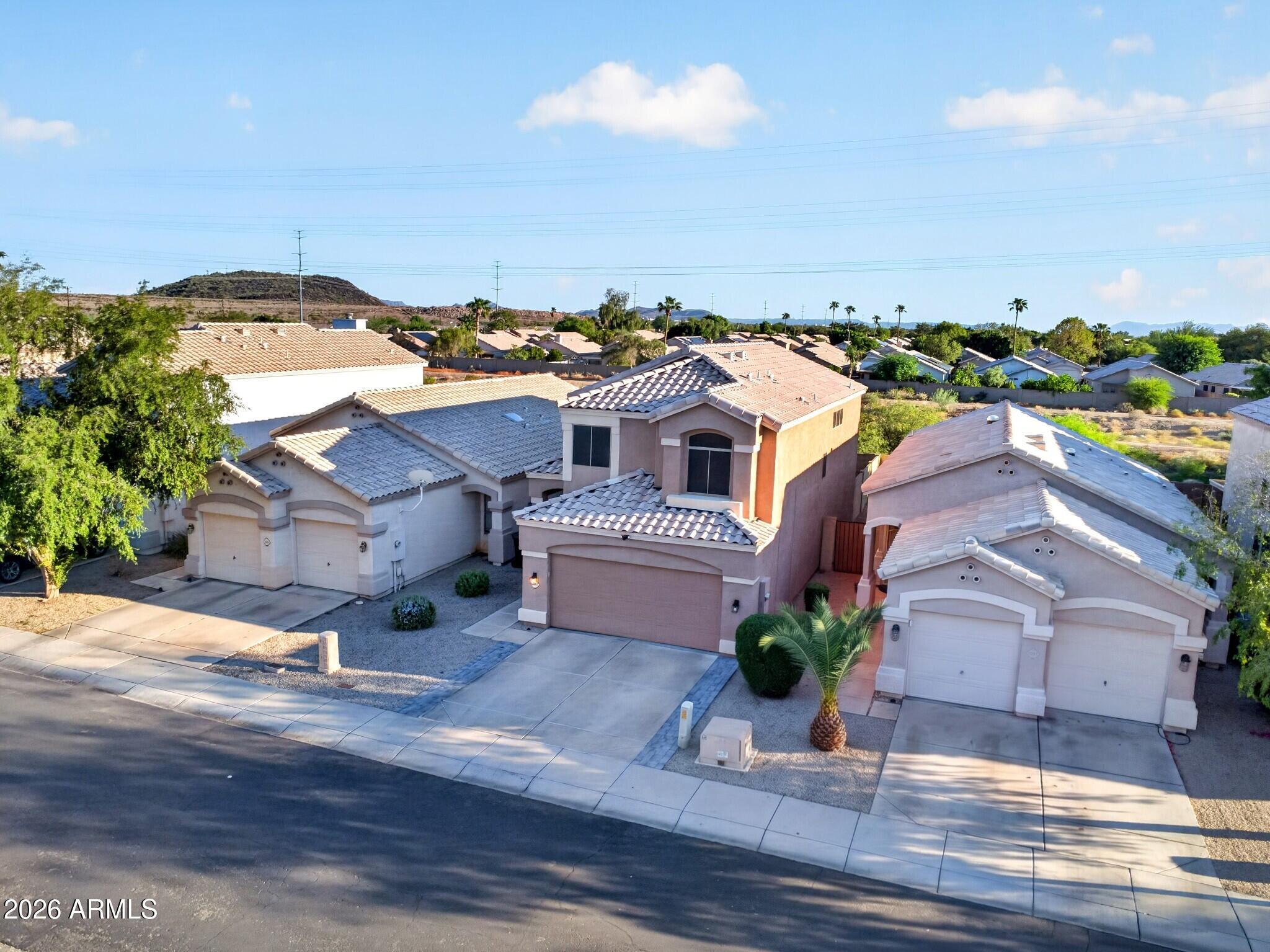 Two-story stucco home with a tiled roof, attached garage, and desert landscaping, photographed from above.