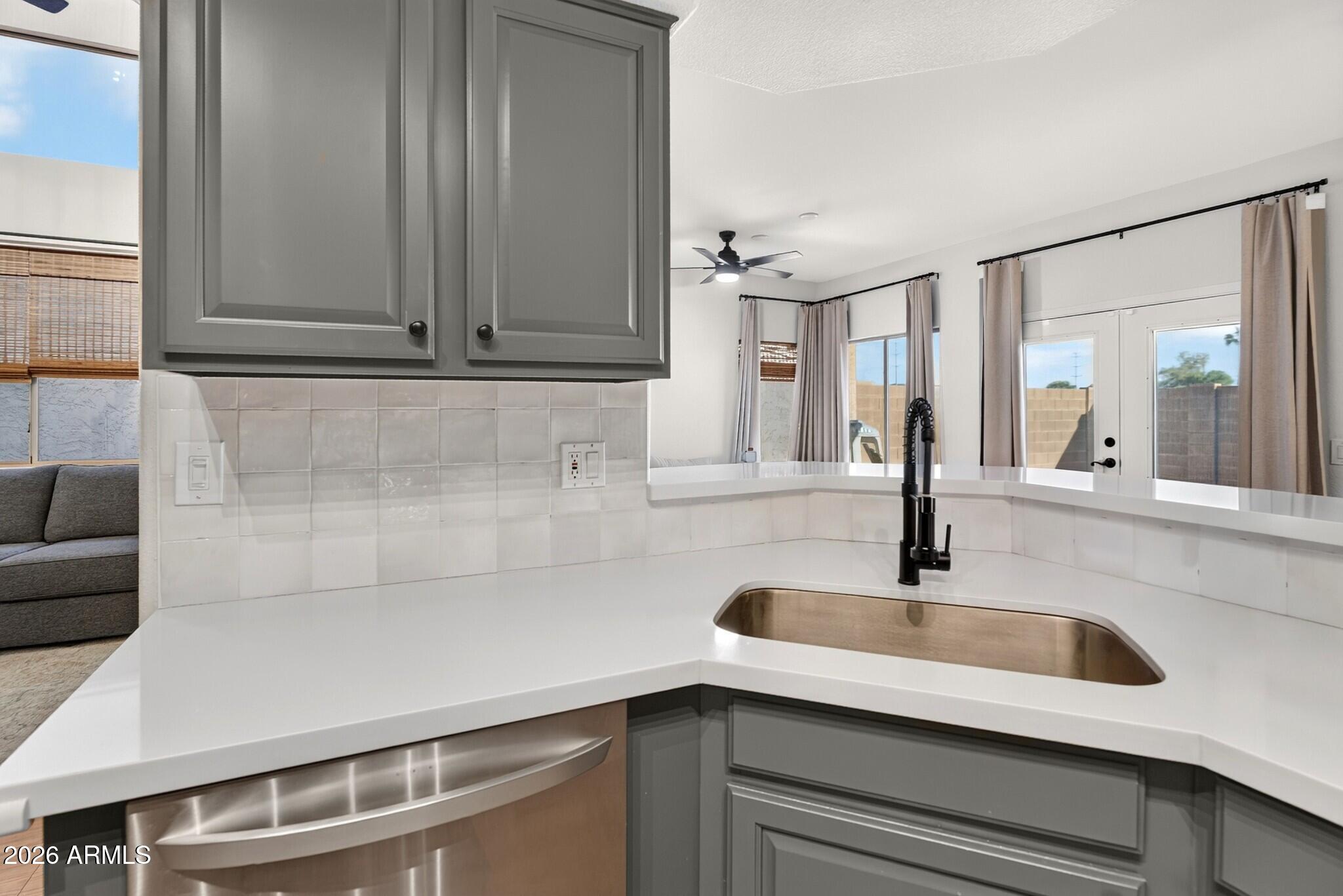 Kitchen with gray cabinets, white countertops, and a large sink beneath glass doors.