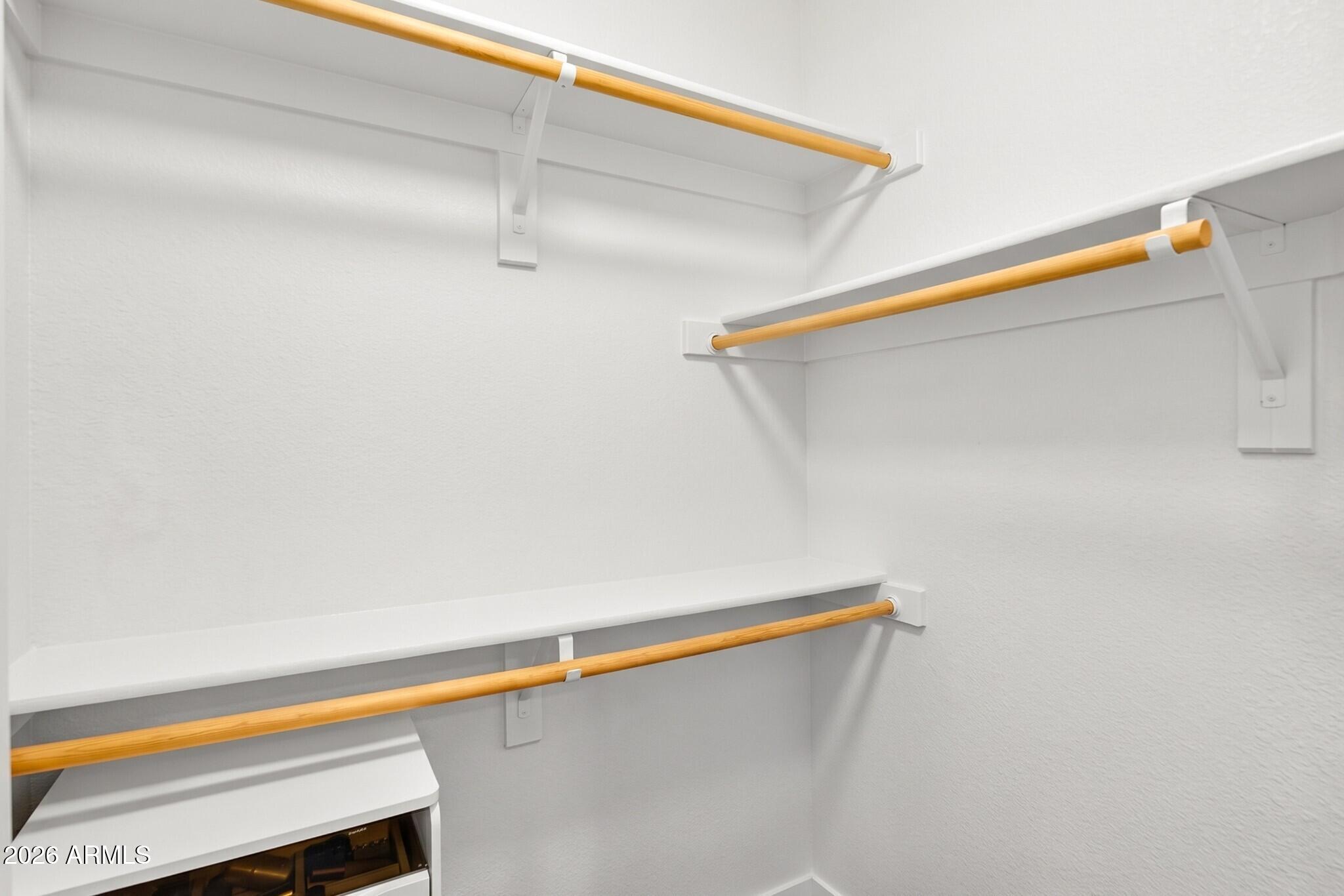 White closet with built-in shelves and wooden hanging rods.