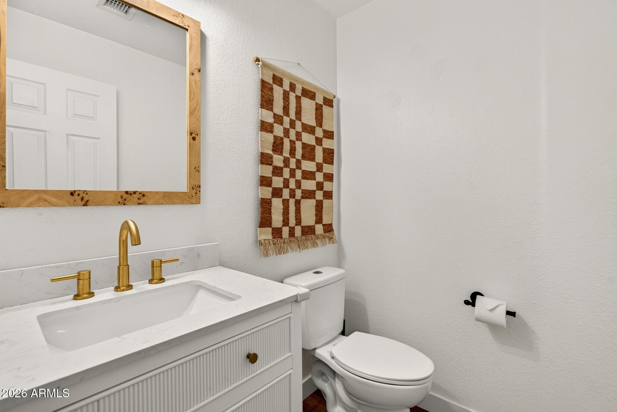 Bathroom with a white fluted vanity, gold fixtures, wood-framed mirror, and woven wall hanging.