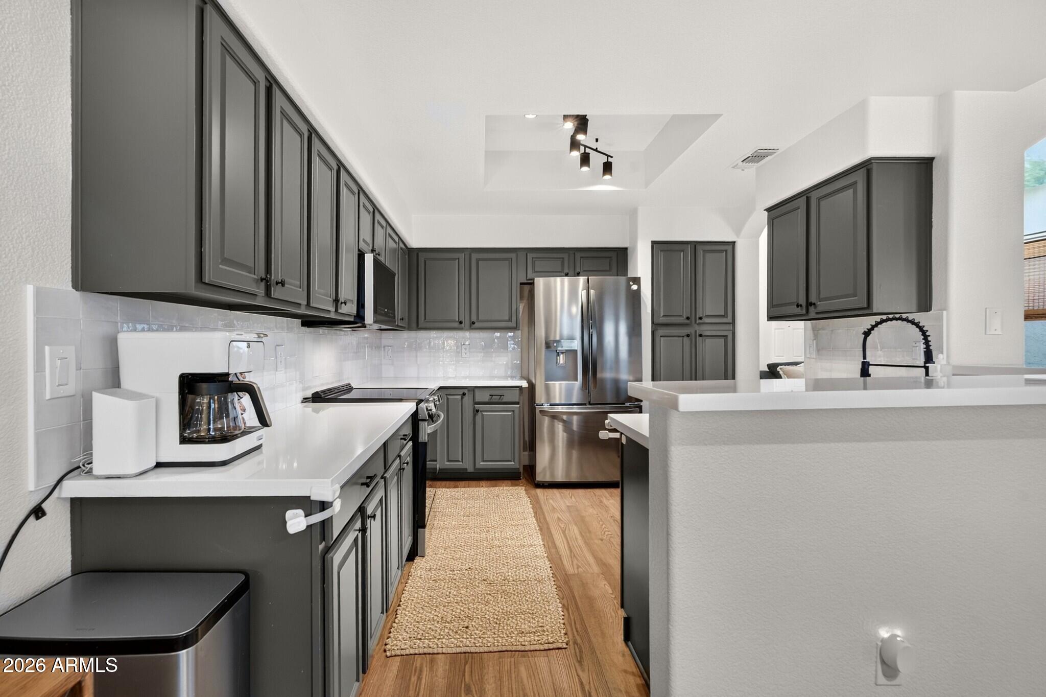 Kitchen with dark gray cabinets, stainless steel appliances, white counters, and a woven runner.