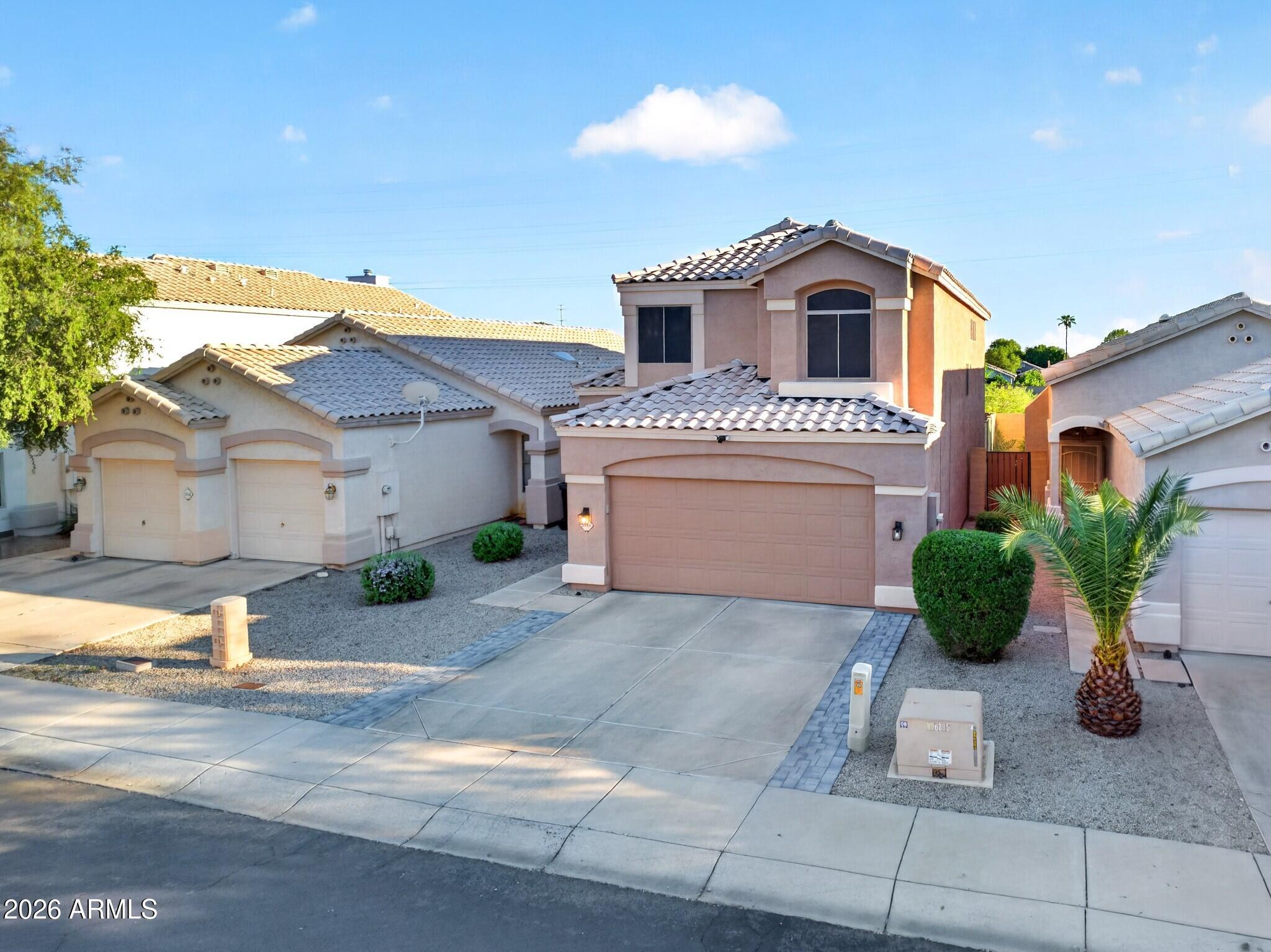 Two-story stucco home with a tile roof, attached garage, and gravel landscaping.