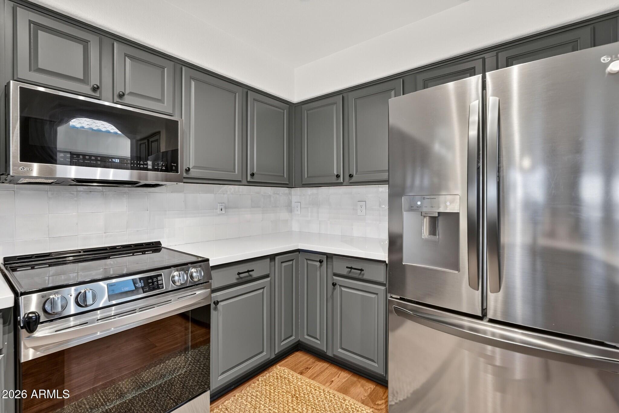 Kitchen with gray cabinets, stainless steel appliances, and a white tile backsplash.