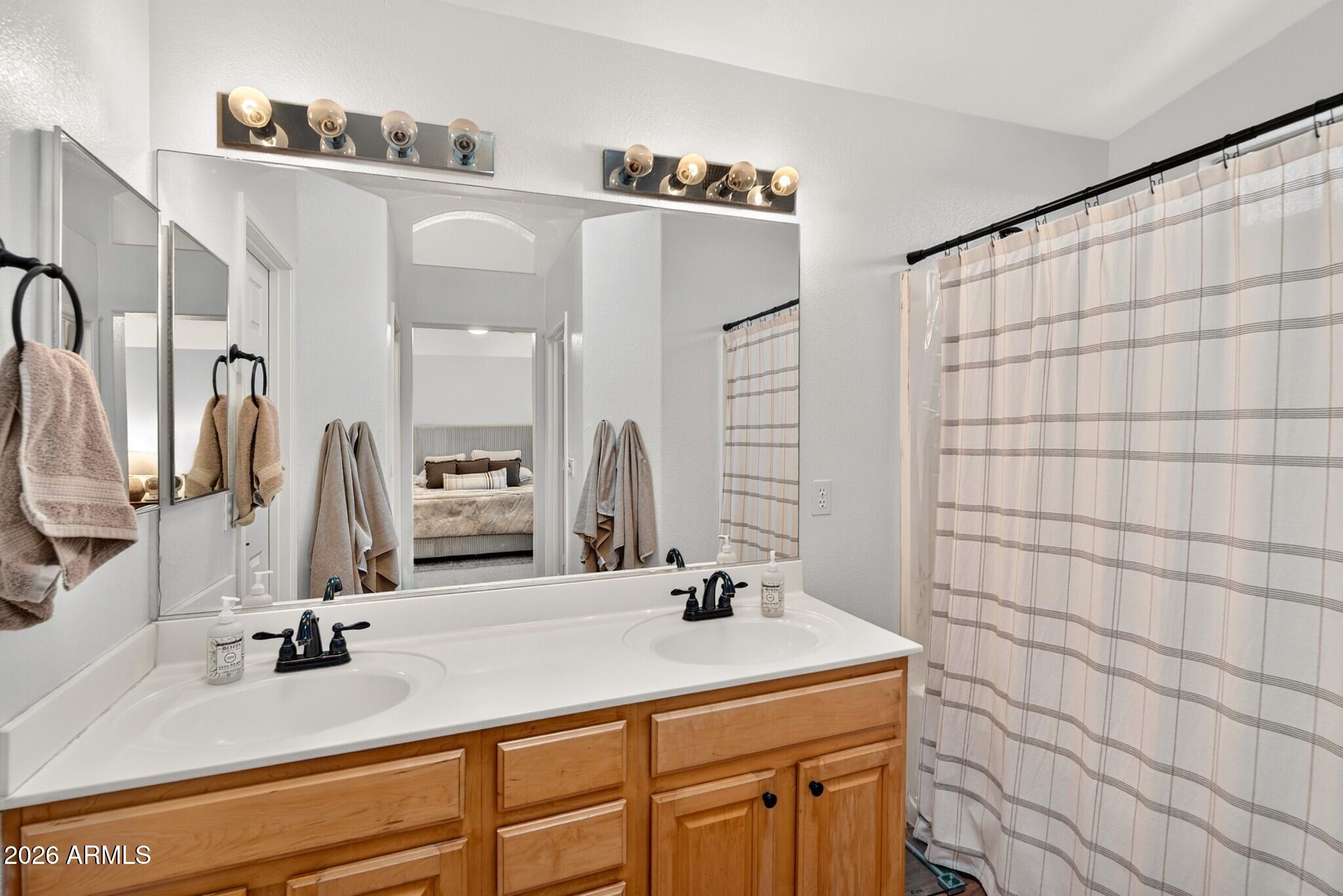 Bathroom with a double-sink vanity, wood cabinets, large mirrors, and a striped shower curtain.