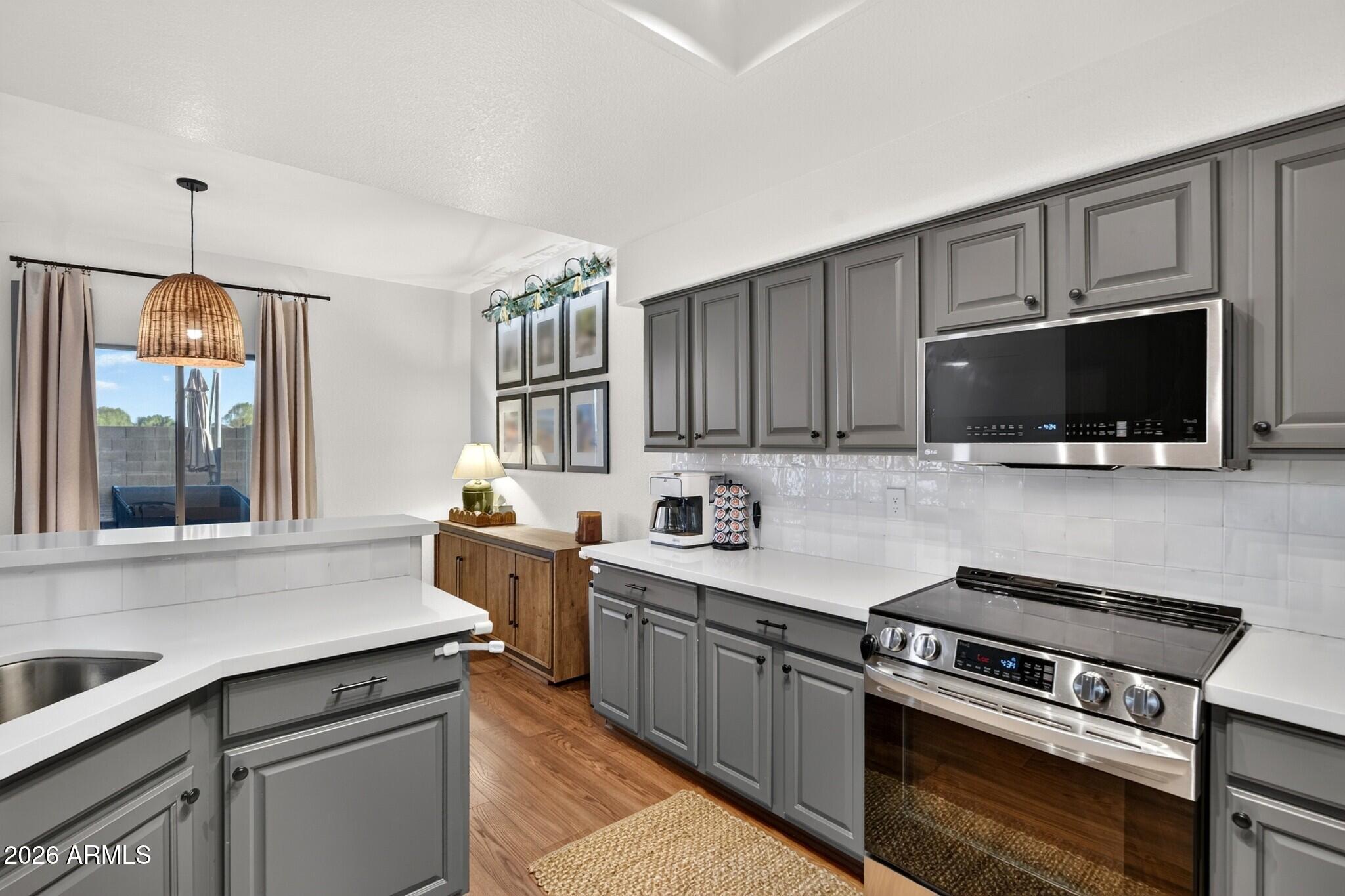 Kitchen with gray cabinets, white countertops, a large sink island, and stainless steel appliances.