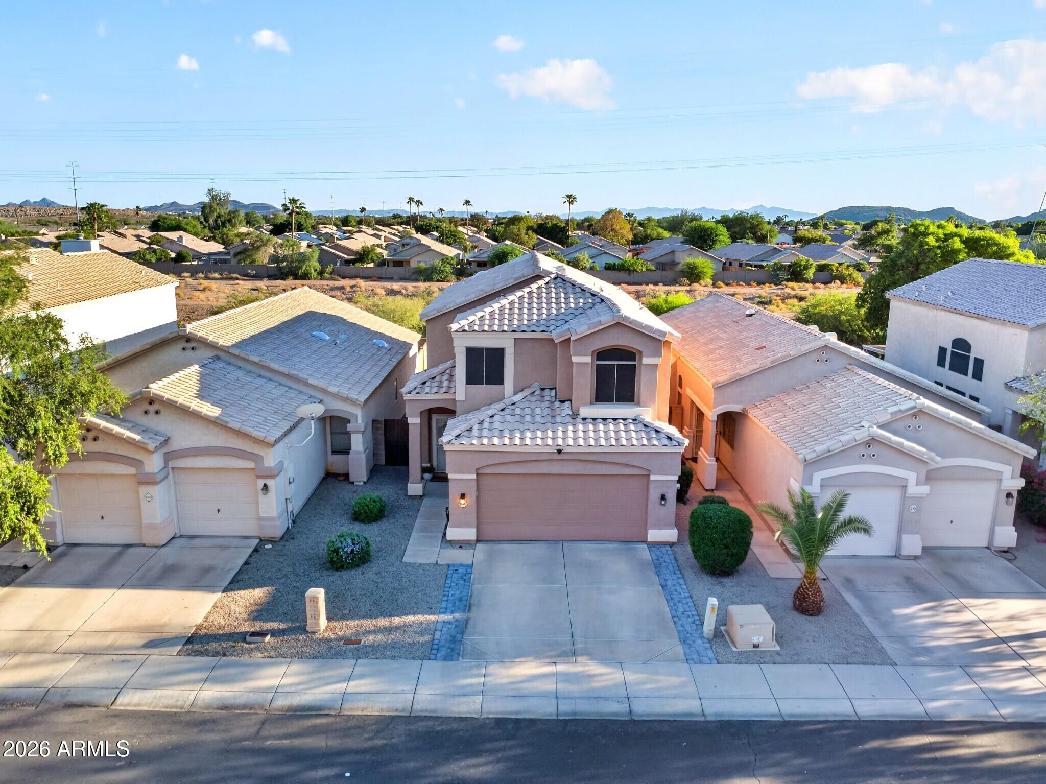 Two-story stucco home with tiled roof, attached garage, gravel landscaping, and distant mountain views.