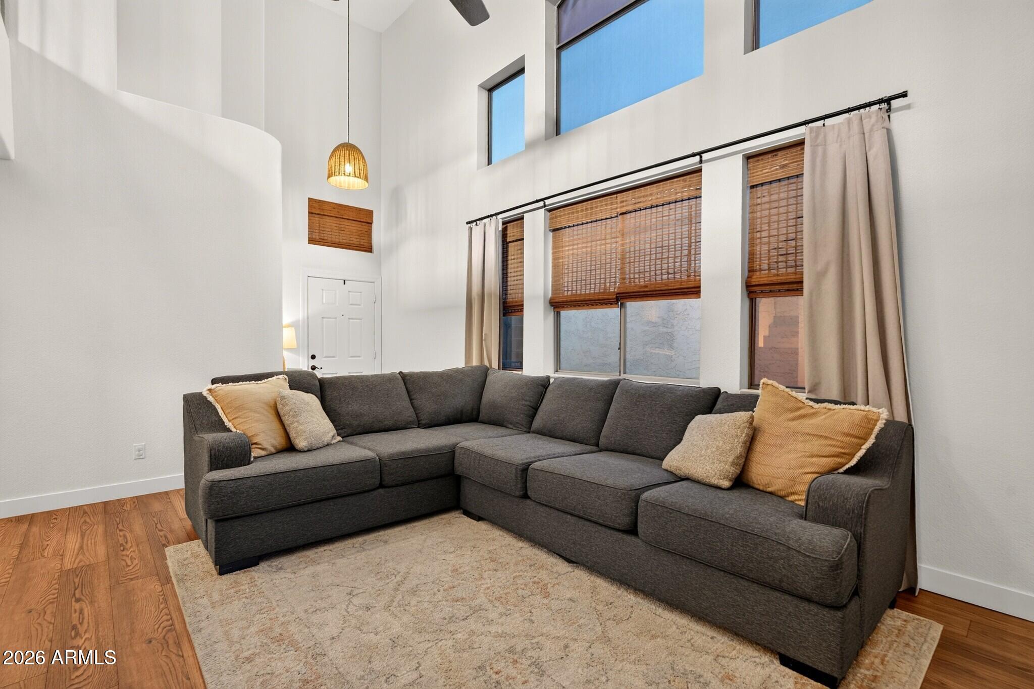 Living room with a charcoal sectional beneath tall windows with woven wood blinds.