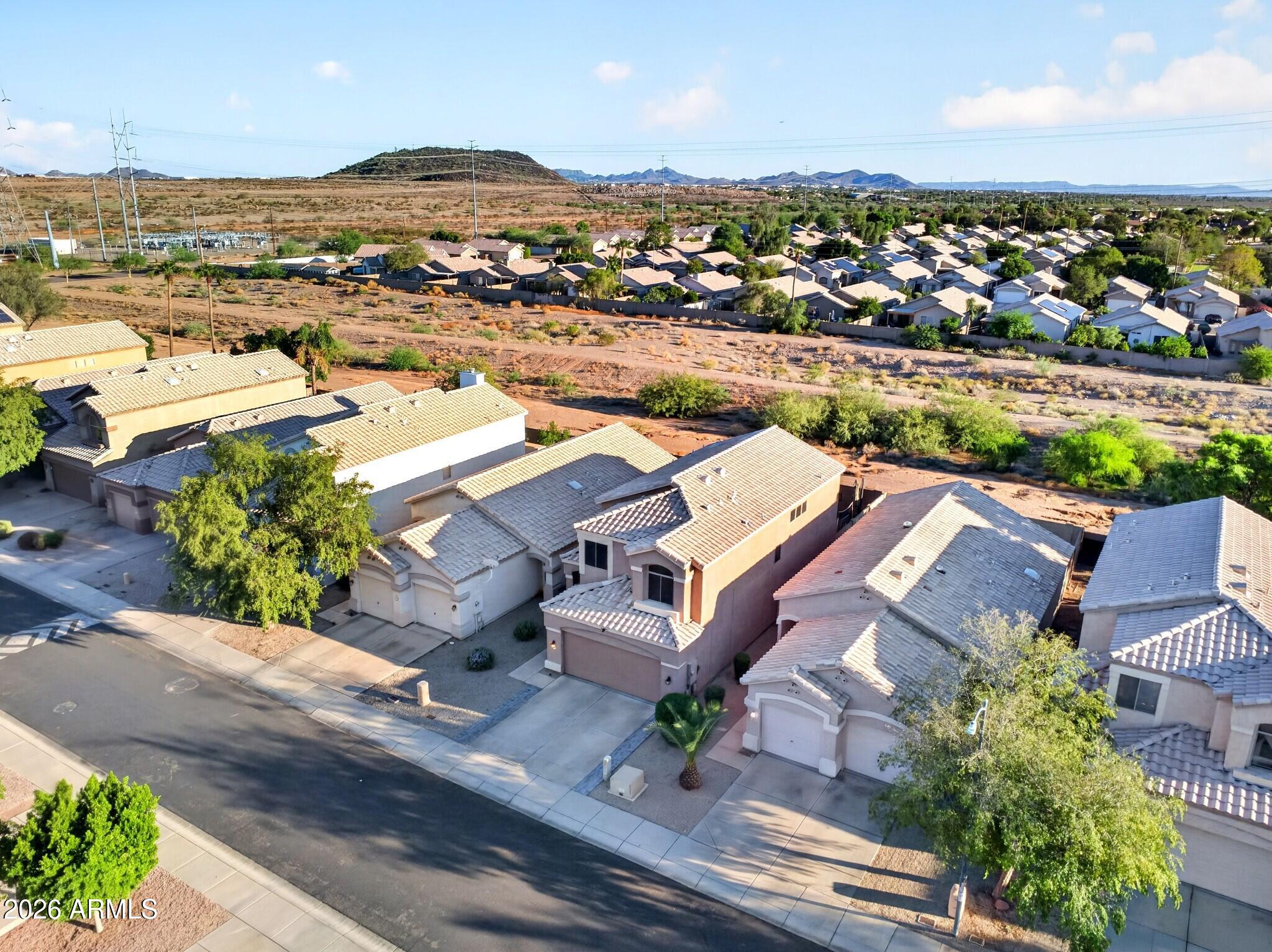 Aerial view of tiled-roof homes beside a desert wash, with distant hills beyond.