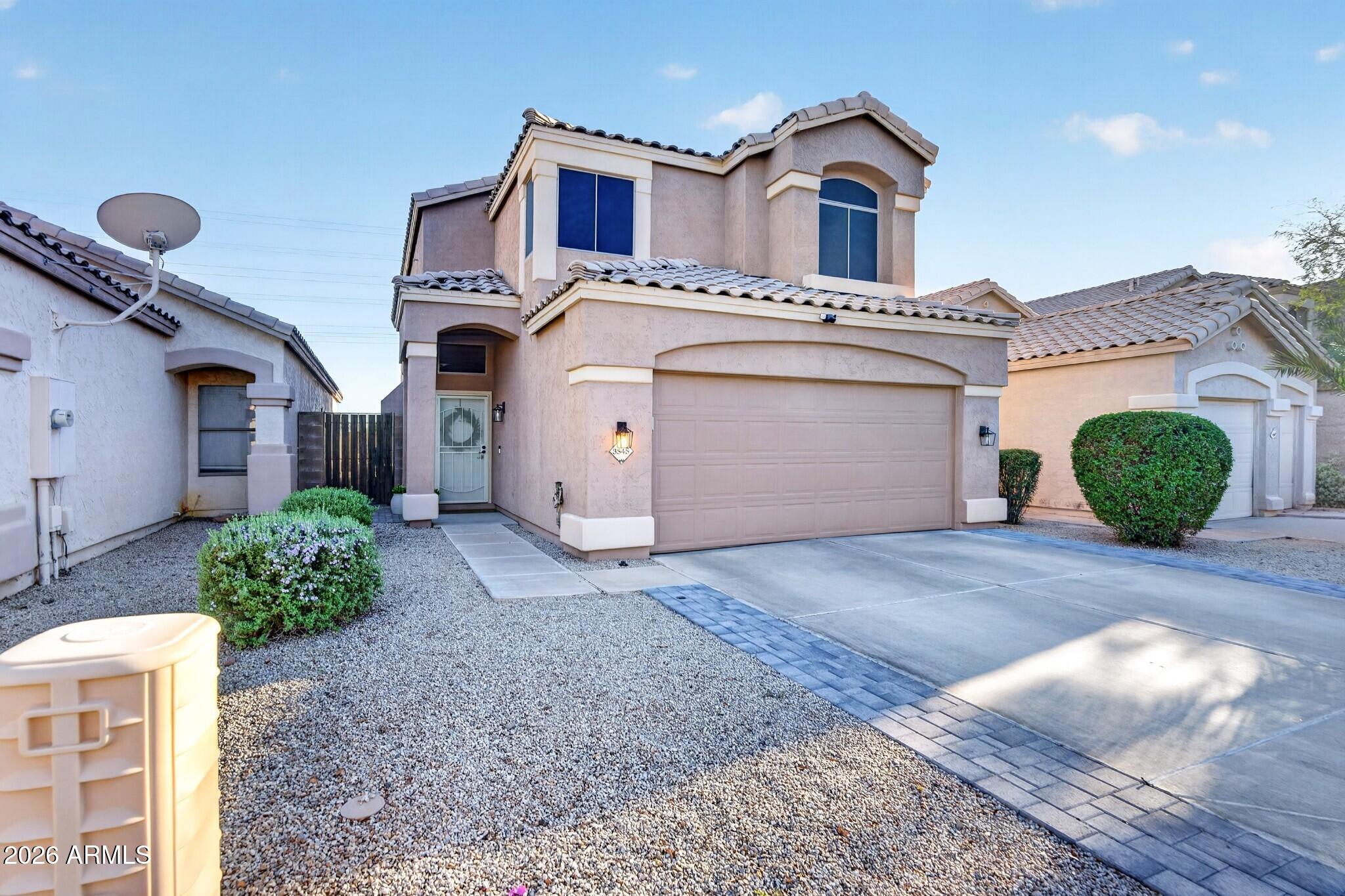 Two-story stucco home with a tile roof, arched windows, gravel landscaping, and a wide two-car garage.
