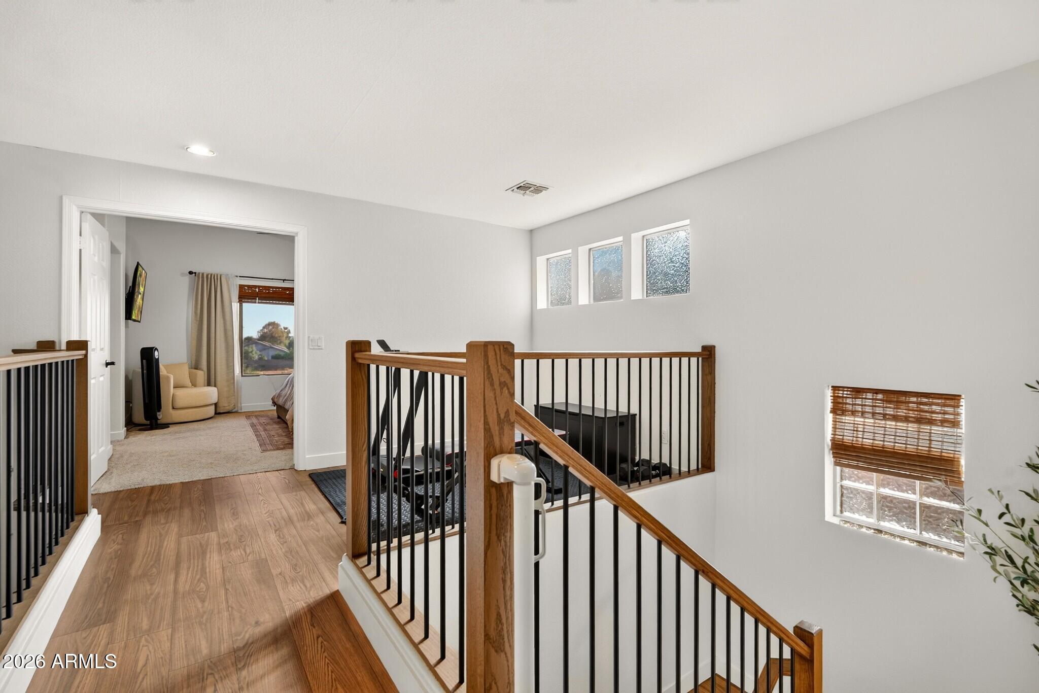 Upstairs landing with wood flooring, a black-and-wood staircase railing, and three high windows.