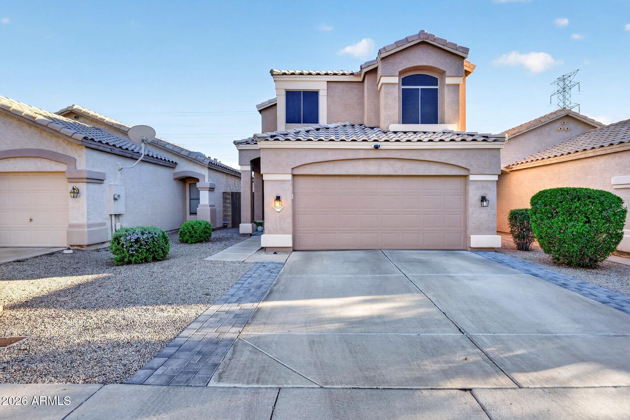 Two-story stucco house with a tile roof, double garage, broad driveway, and gravel landscaping.