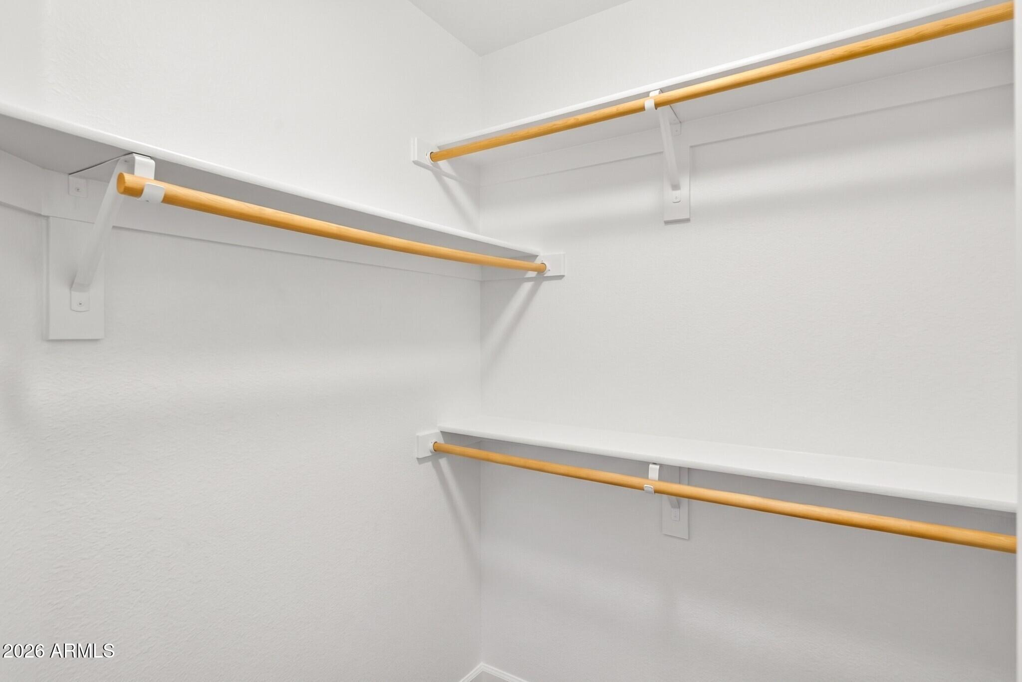 White walk-in closet with multiple wooden hanging rods and shelves.