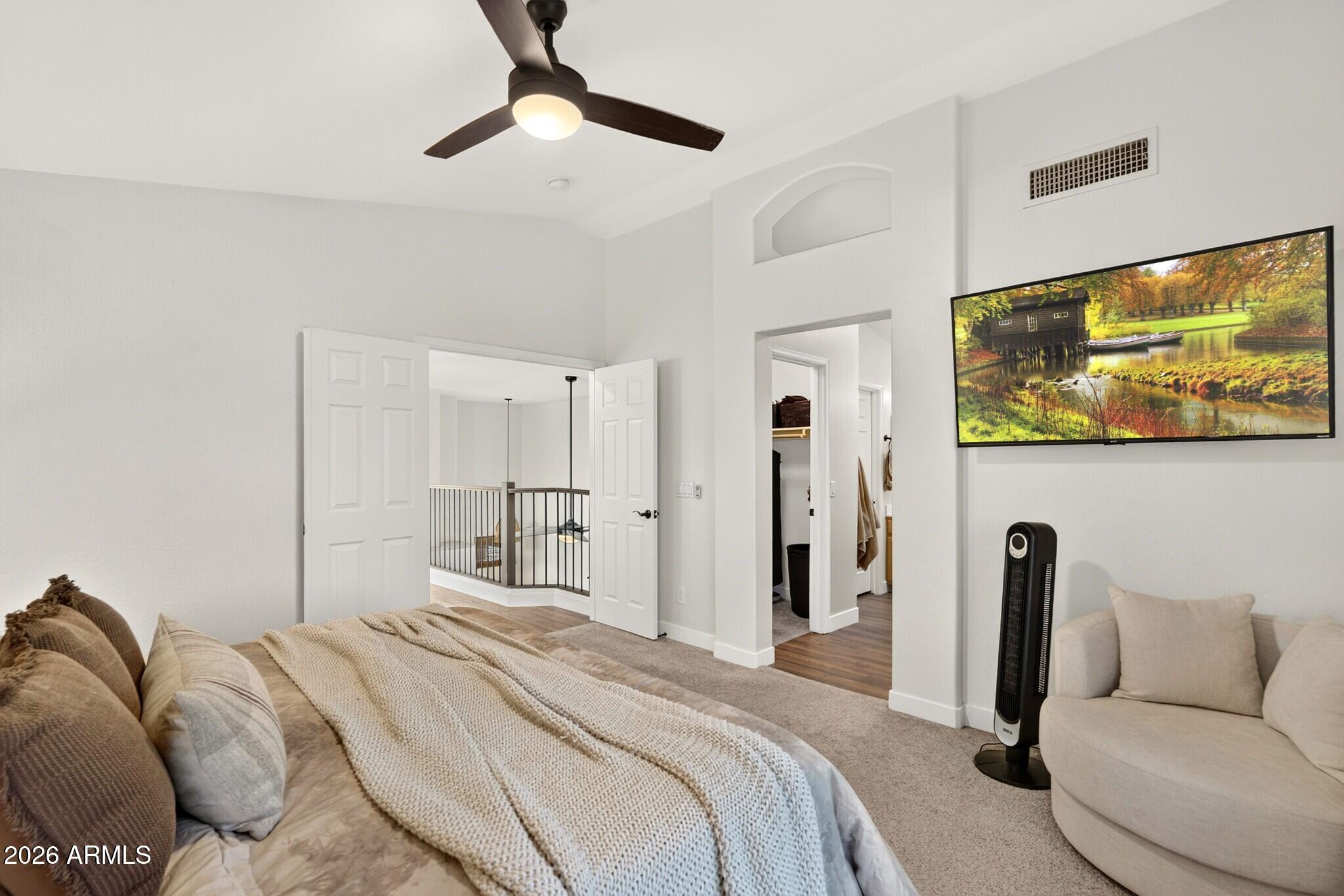 Furnished bedroom with a ceiling fan and open doors overlooking a railed landing.