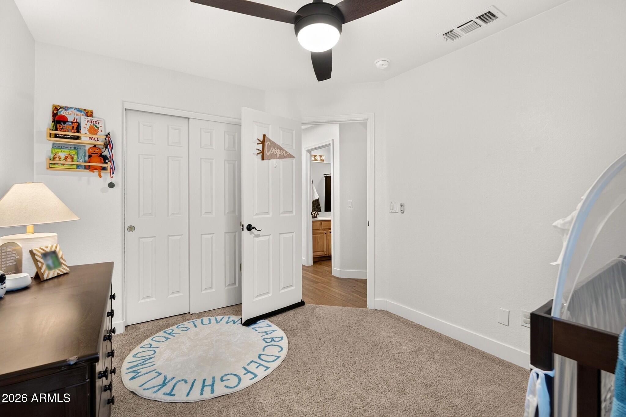Child’s bedroom with a round alphabet rug, white closet doors, and a crib at the edge.