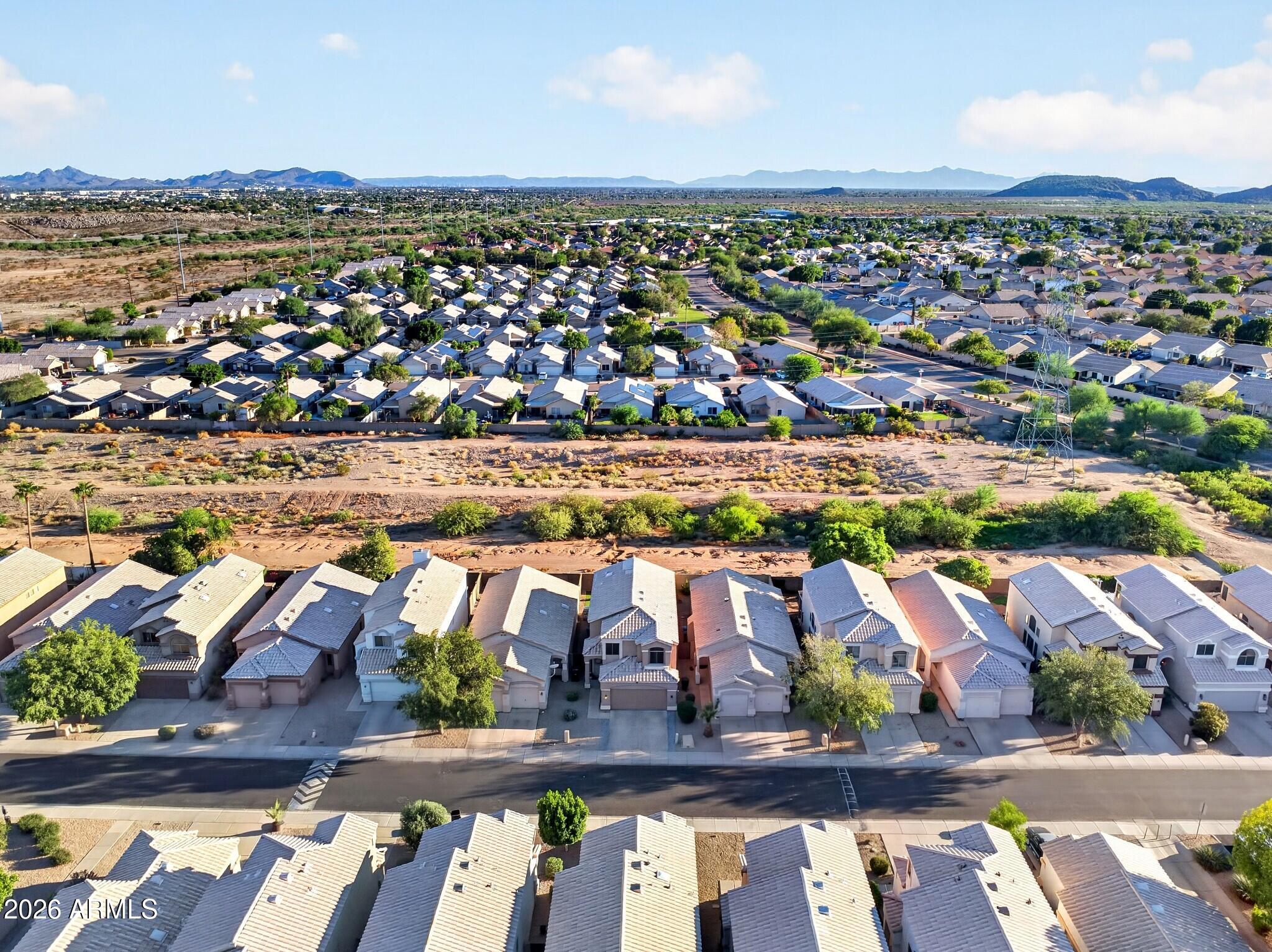 Aerial neighborhood view with rows of homes, a dry wash, and distant mountains.