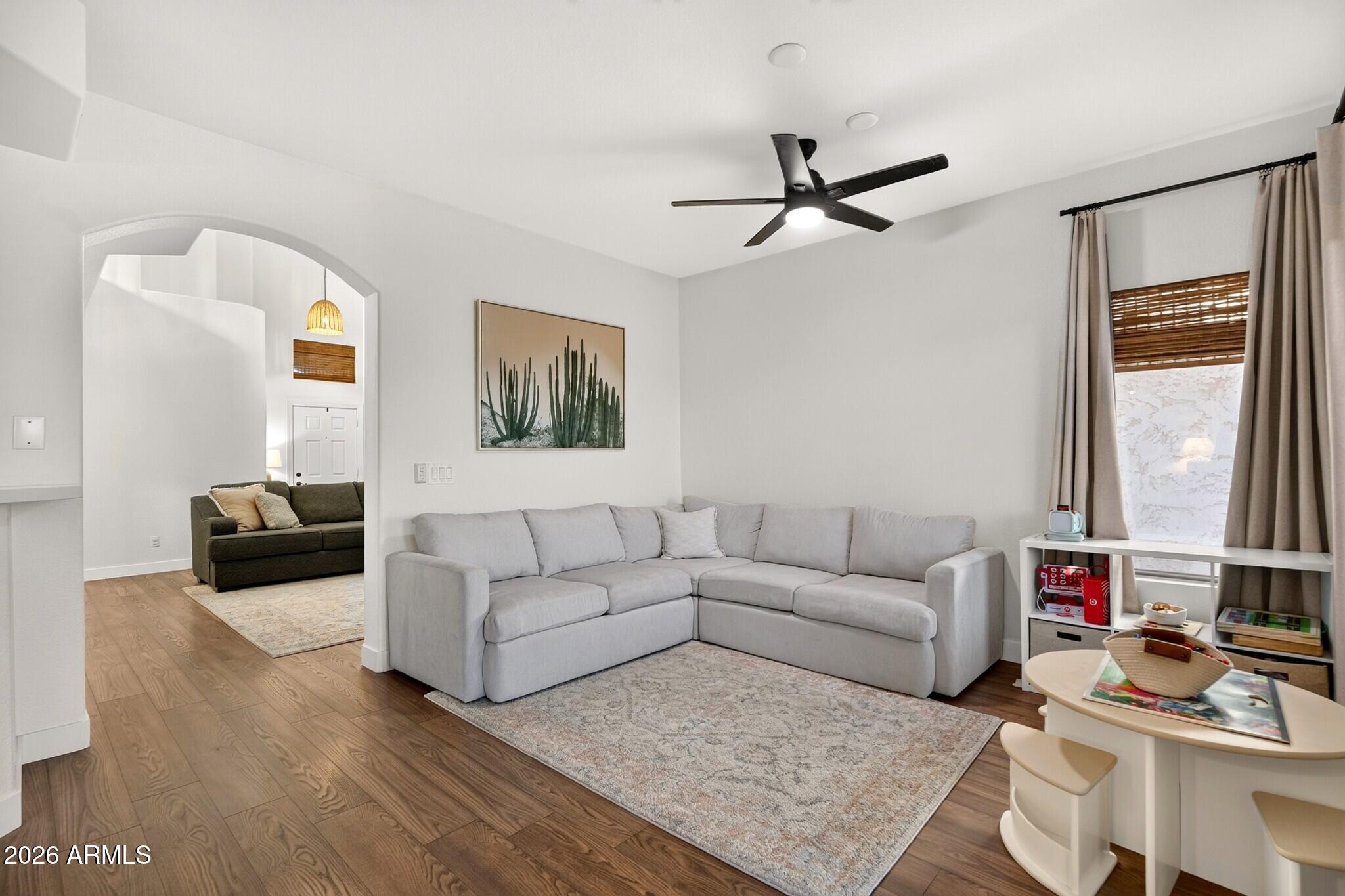 Living room with a large gray sectional, wood floors, black ceiling fan, and arched opening to a second seating area.