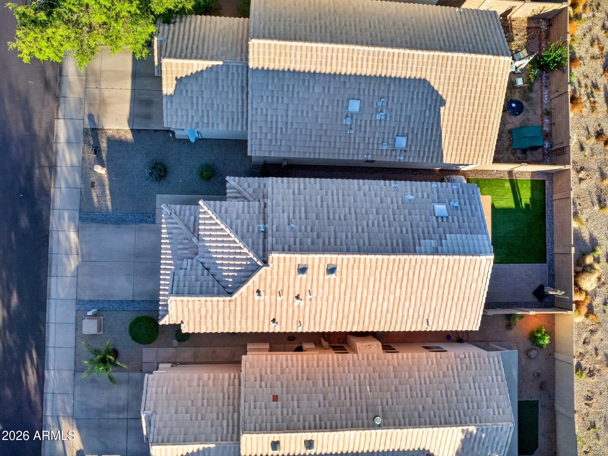 Aerial view of a tan-roofed home with a fenced green-turf backyard and gravel landscaping.