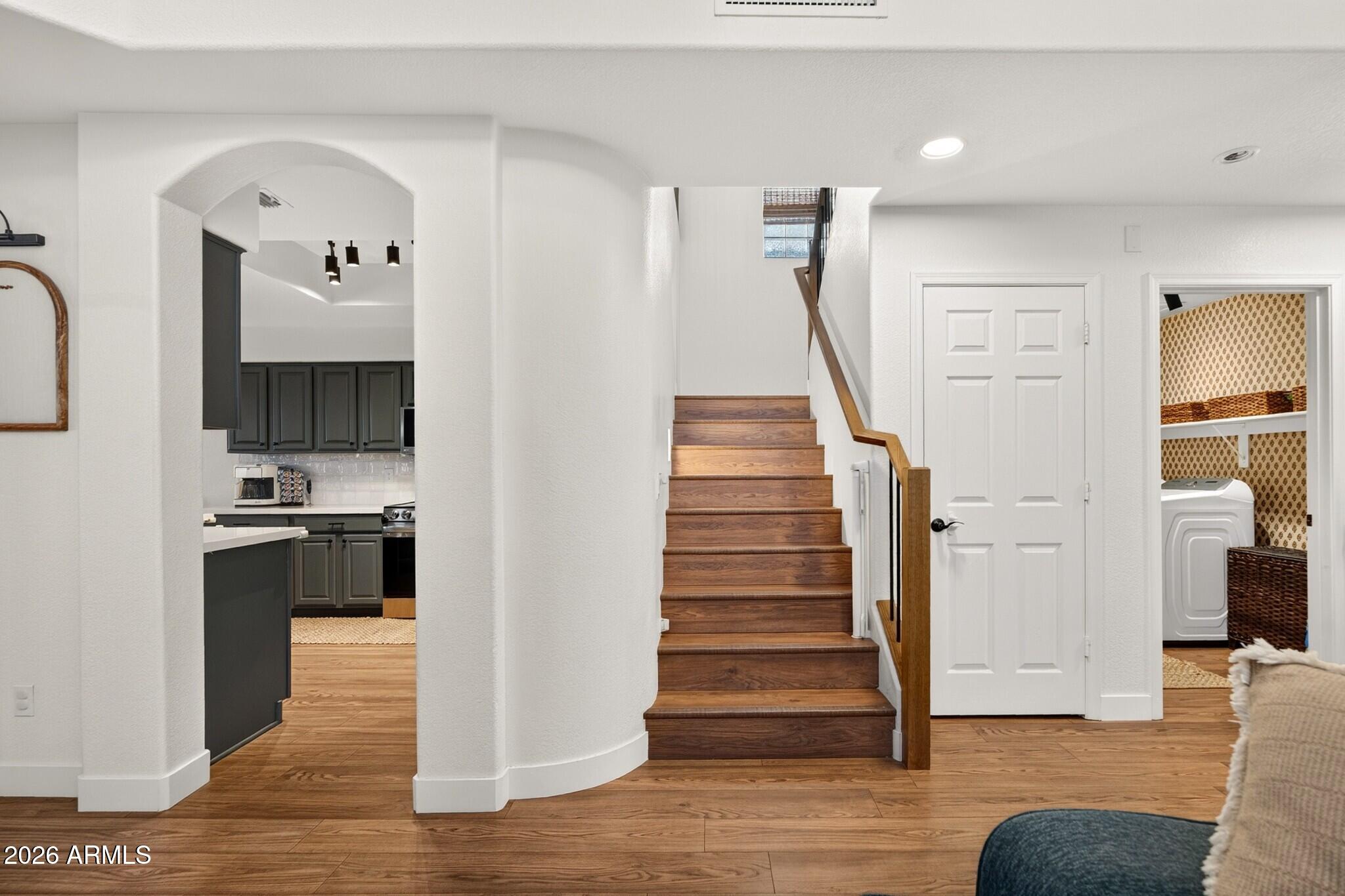 Entryway with a wood staircase, arched kitchen opening, and laundry room doorway.