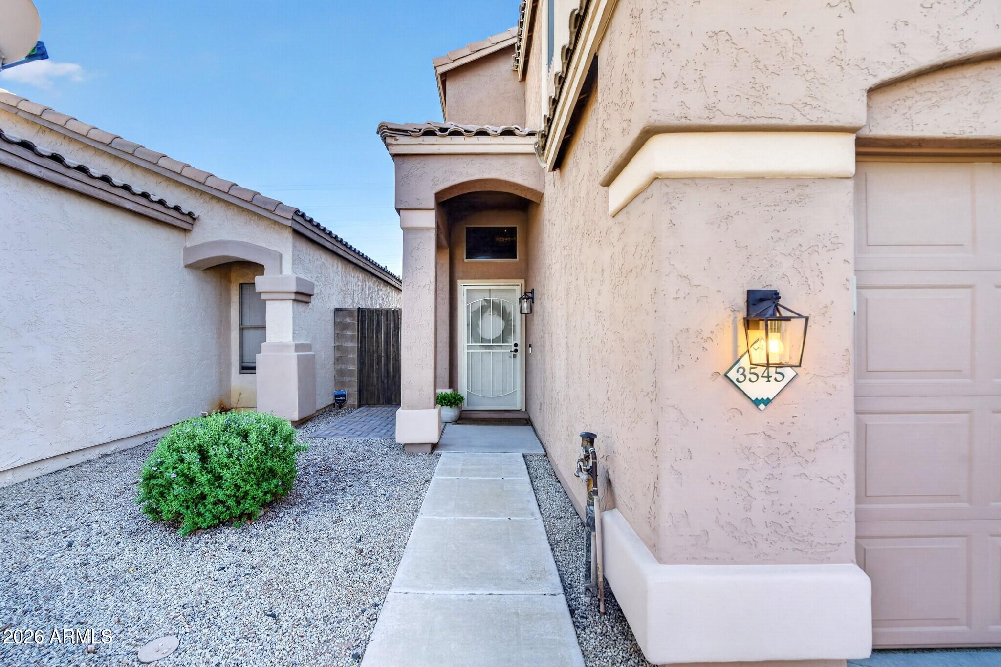 Stucco home entrance with a covered doorway, gravel landscaping, and illuminated 3545 address plaque.