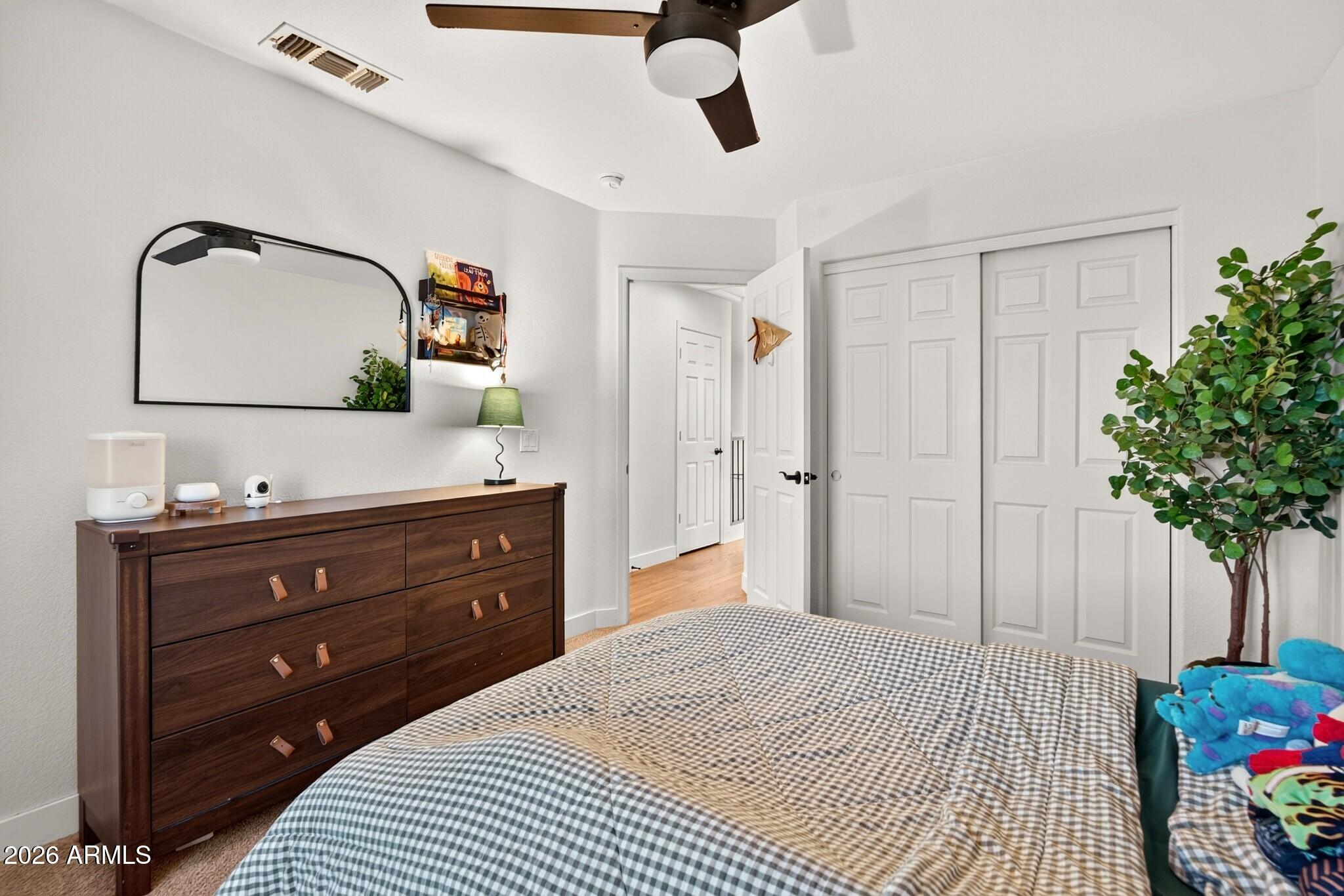 Furnished bedroom with a checkered bed, dark wood dresser, and white closet doors.