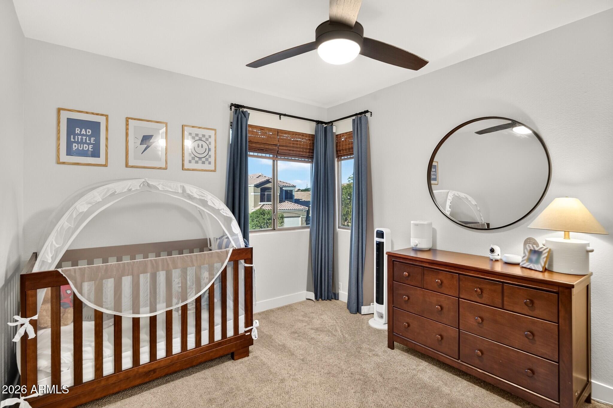 Nursery with a wood crib and mesh canopy, matching dresser, round mirror, and corner windows.