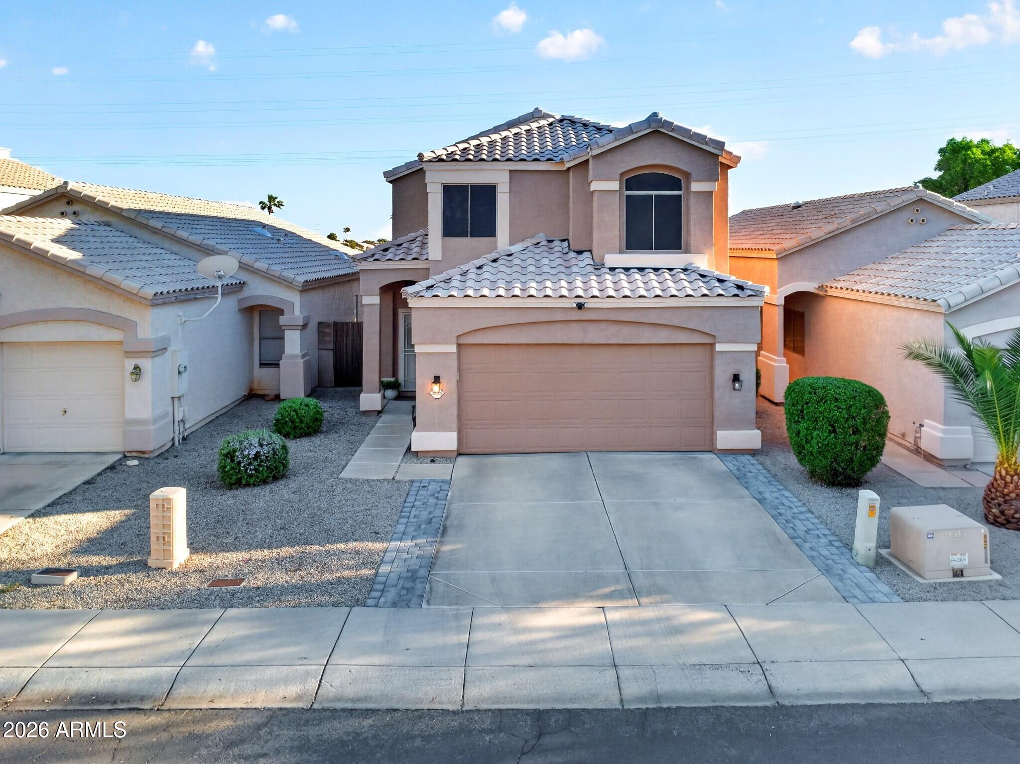 Two-story stucco home with a tiled roof, double garage, gravel landscaping, and a wide driveway.
