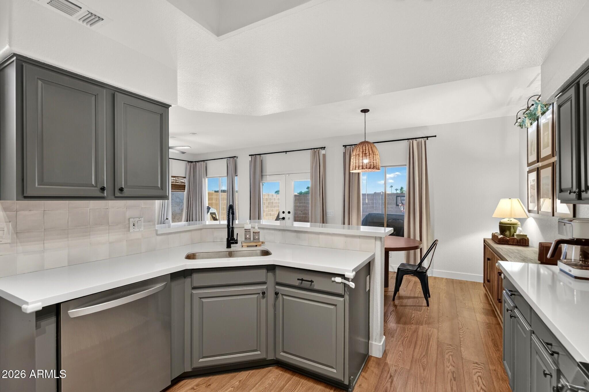 Kitchen with gray cabinets and white counters opening to a dining area with wood flooring.