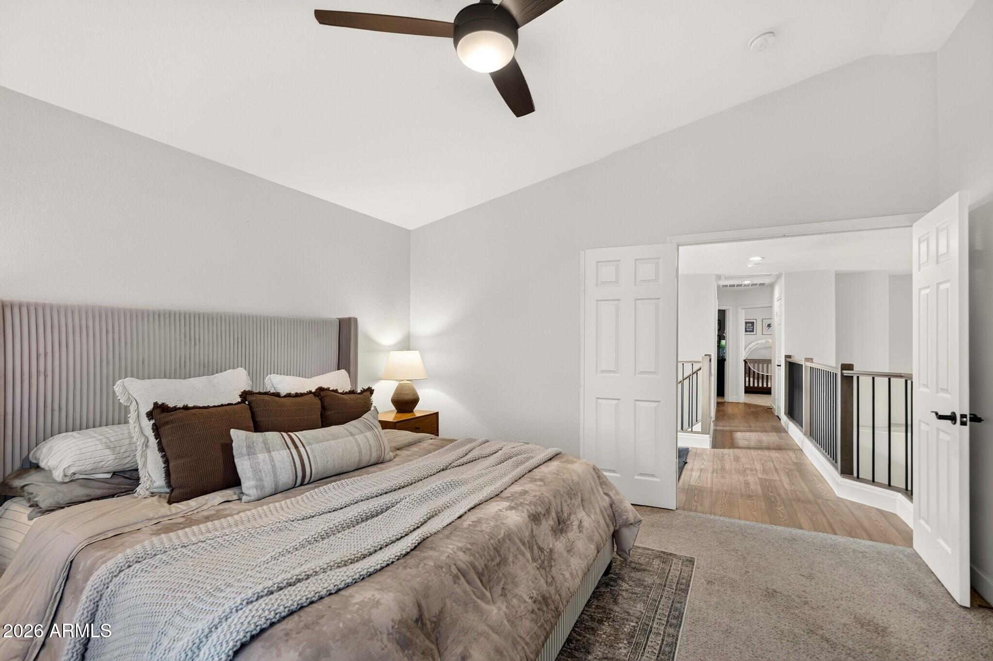 Bedroom with a layered bed and tall upholstered headboard opening onto an upstairs hallway.