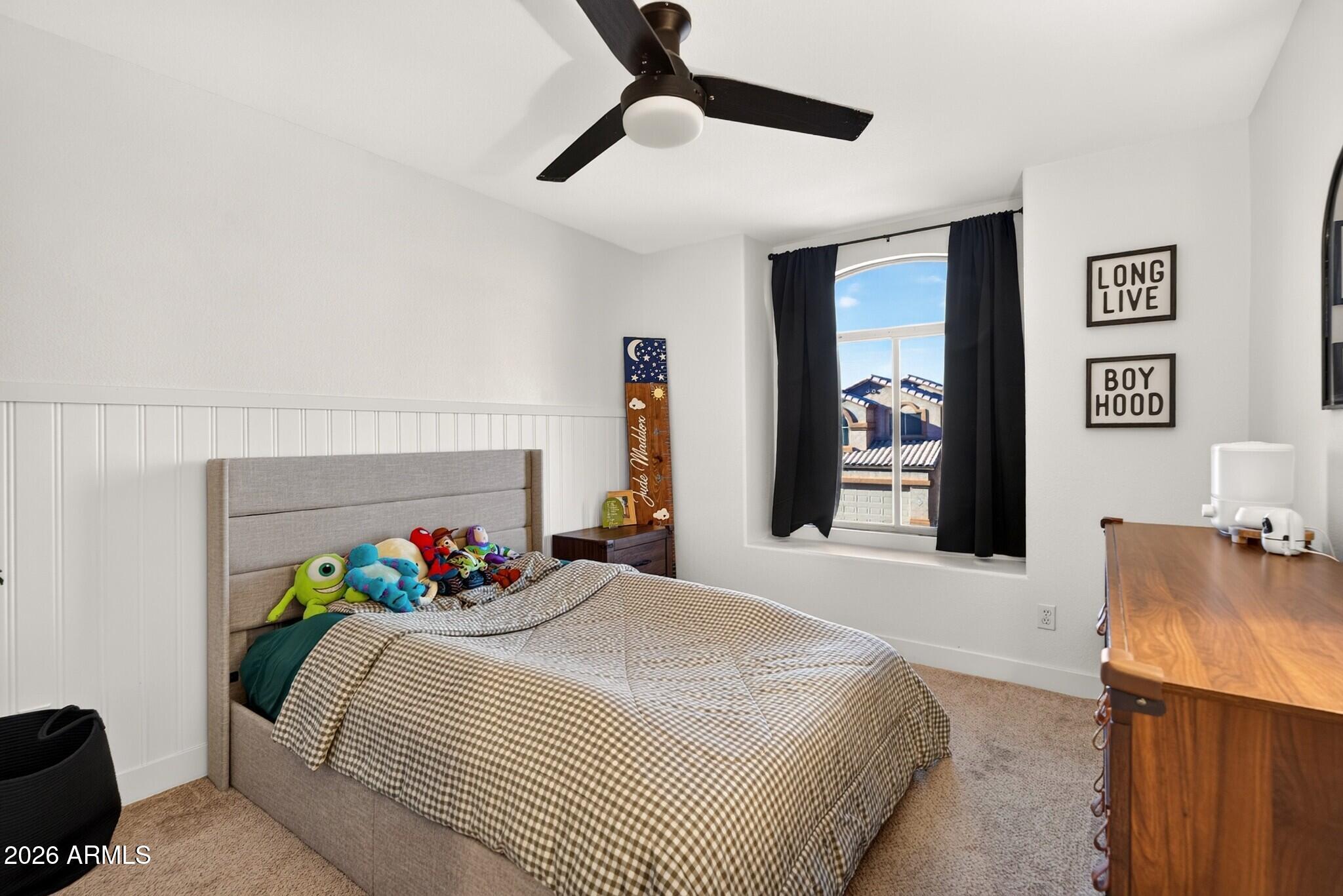 Bedroom with a gray upholstered bed, checkered bedding, stuffed toys, and a window with black curtains.