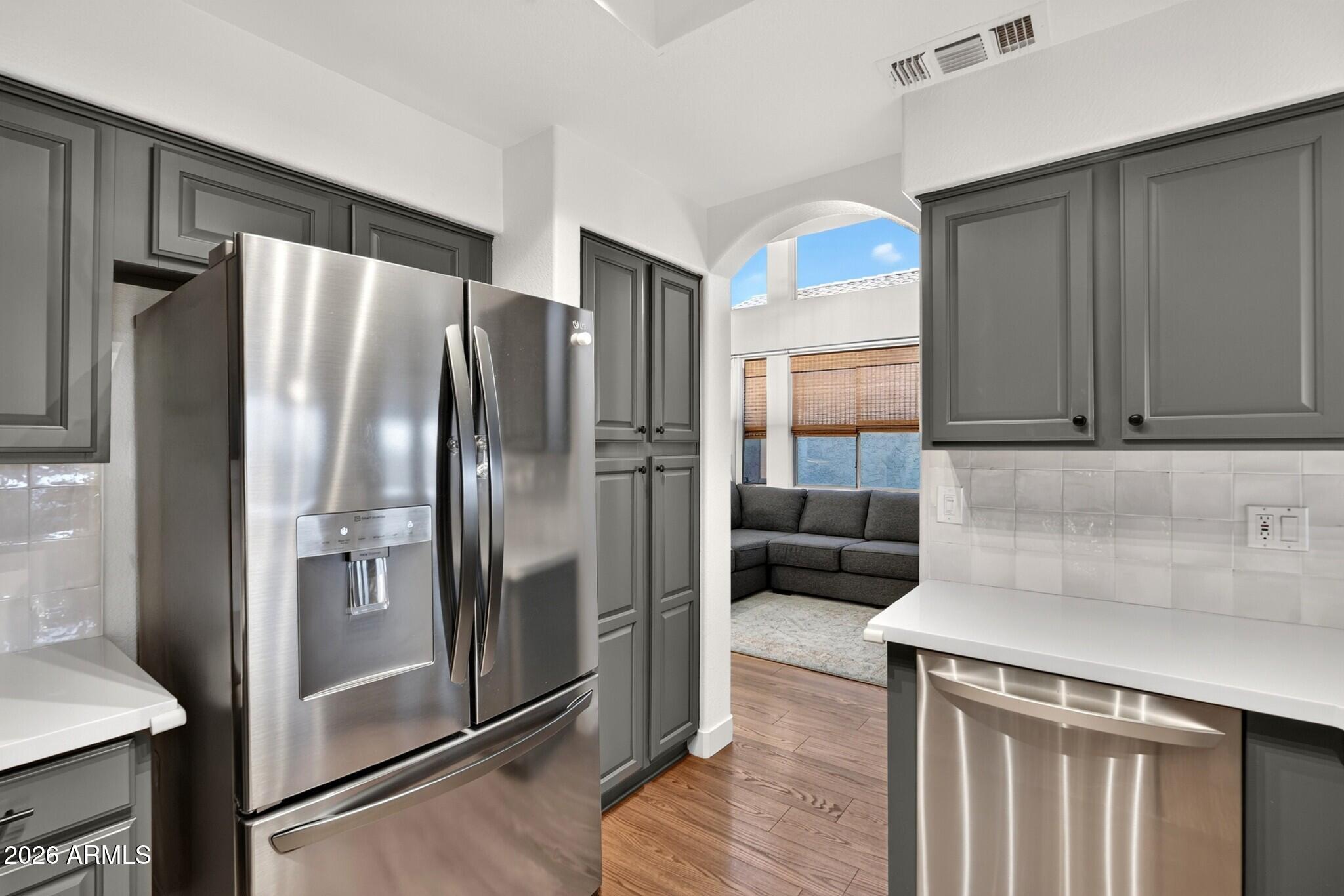Kitchen with gray cabinets and stainless appliances opening onto a living area with a gray sectional.