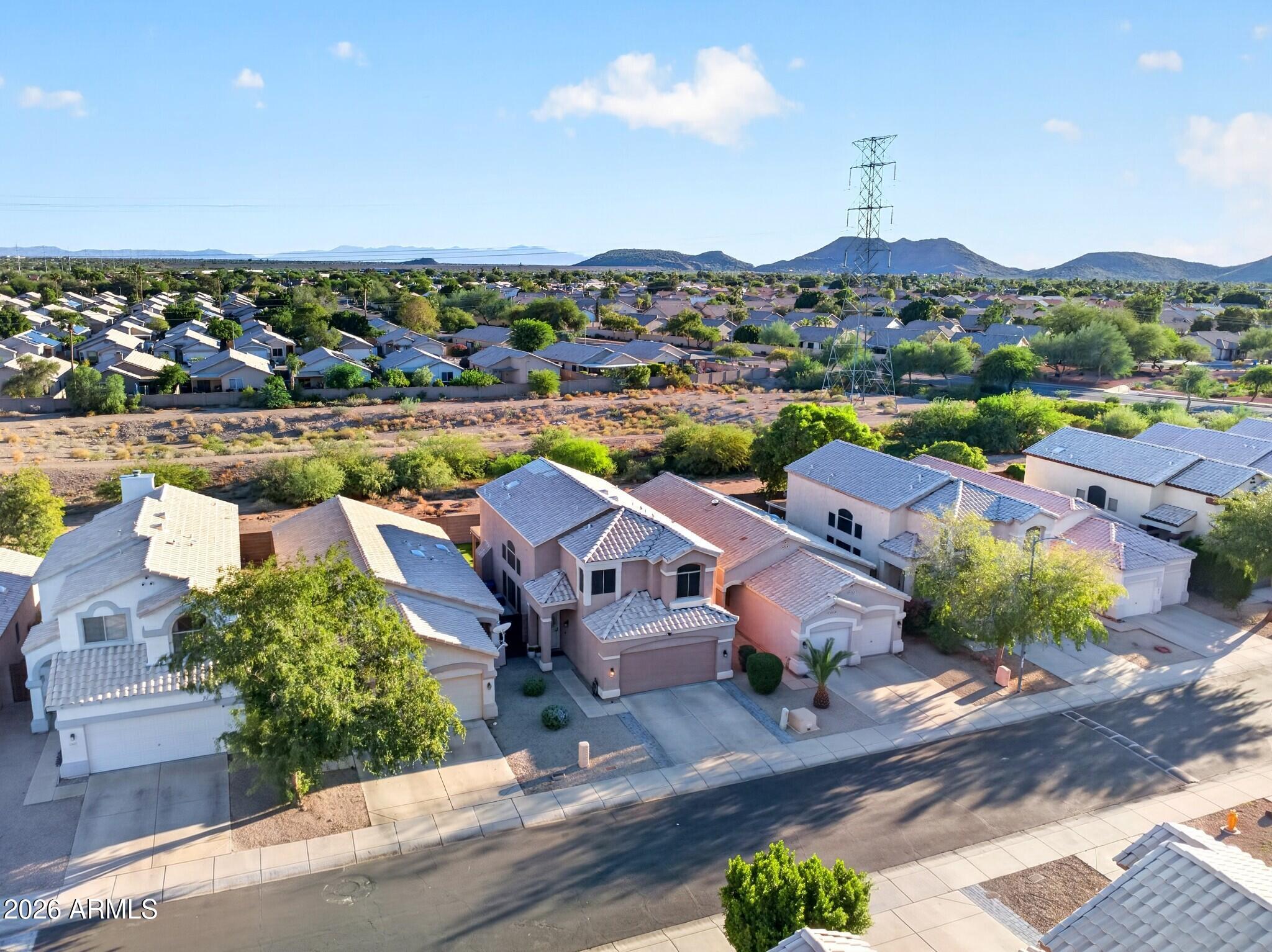 Aerial view of suburban homes, desert mountains, and a transmission tower.