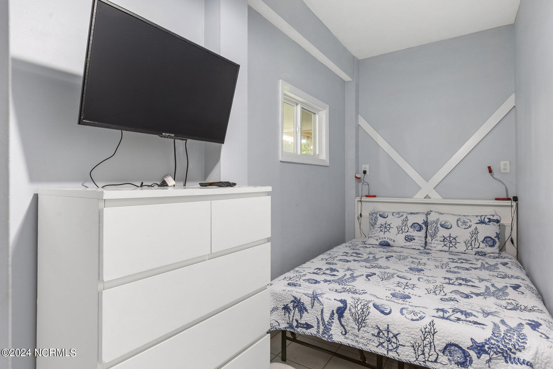 Bedroom with nautical-patterned bedding, a white dresser, and a wall-mounted television.