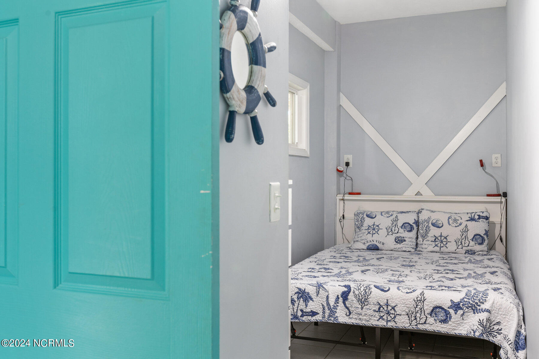 Bedroom with nautical-patterned bedding, gray walls, and an open turquoise door.