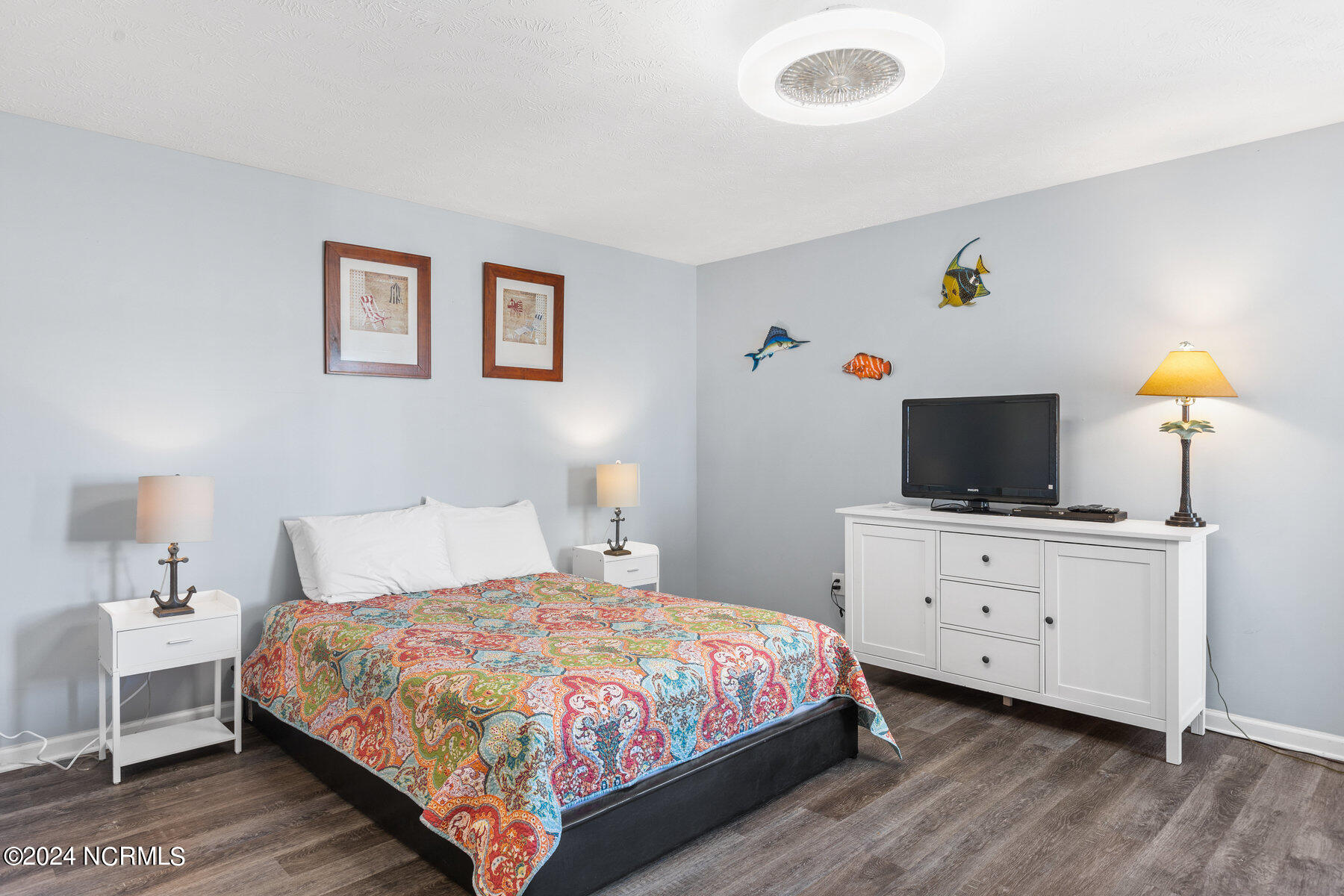 Furnished bedroom with a colorful patterned quilt and fish decorations above a television.
