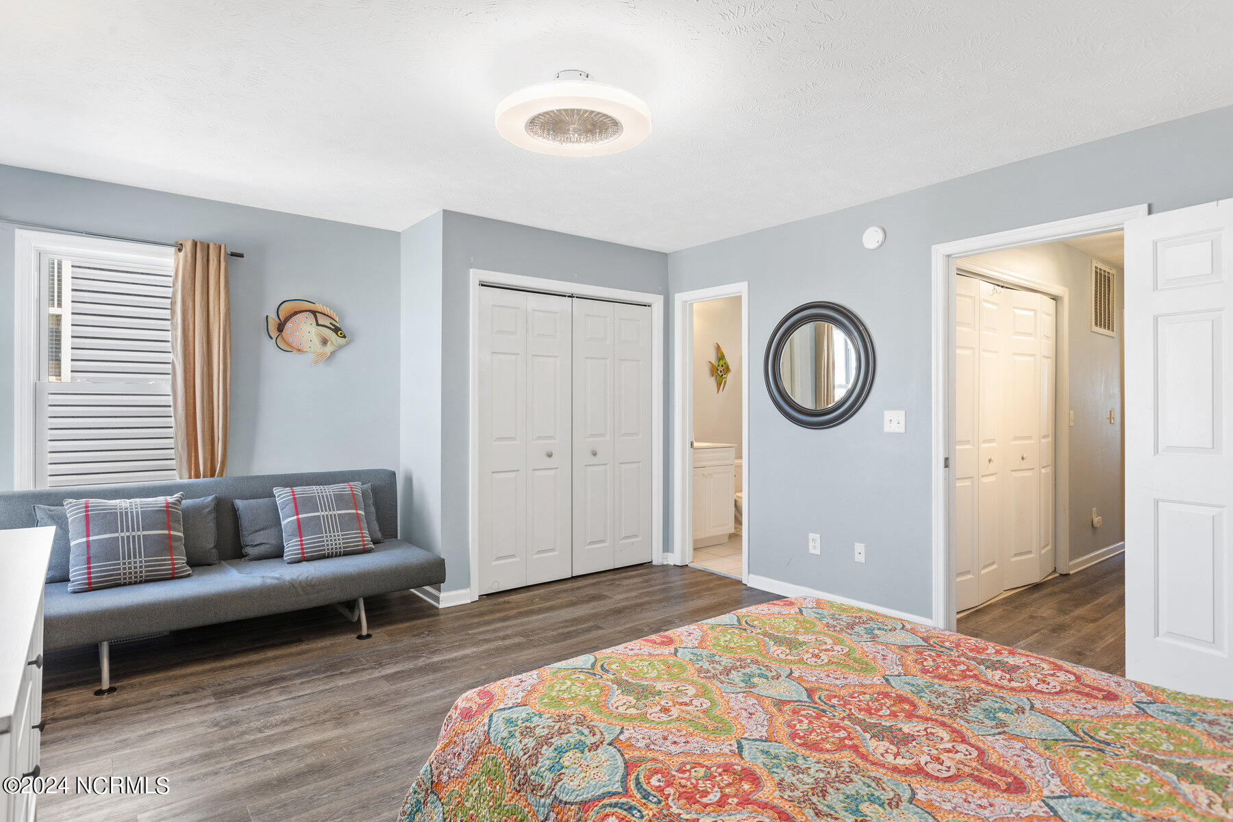 Bedroom with a colorful patterned bedspread, gray sofa, and pale blue walls.