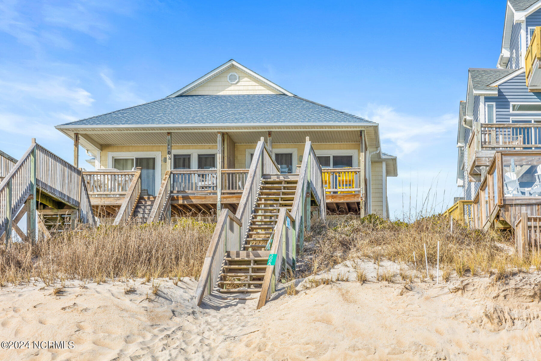 Beach house with raised wooden decks and stairs descending through sandy dunes.