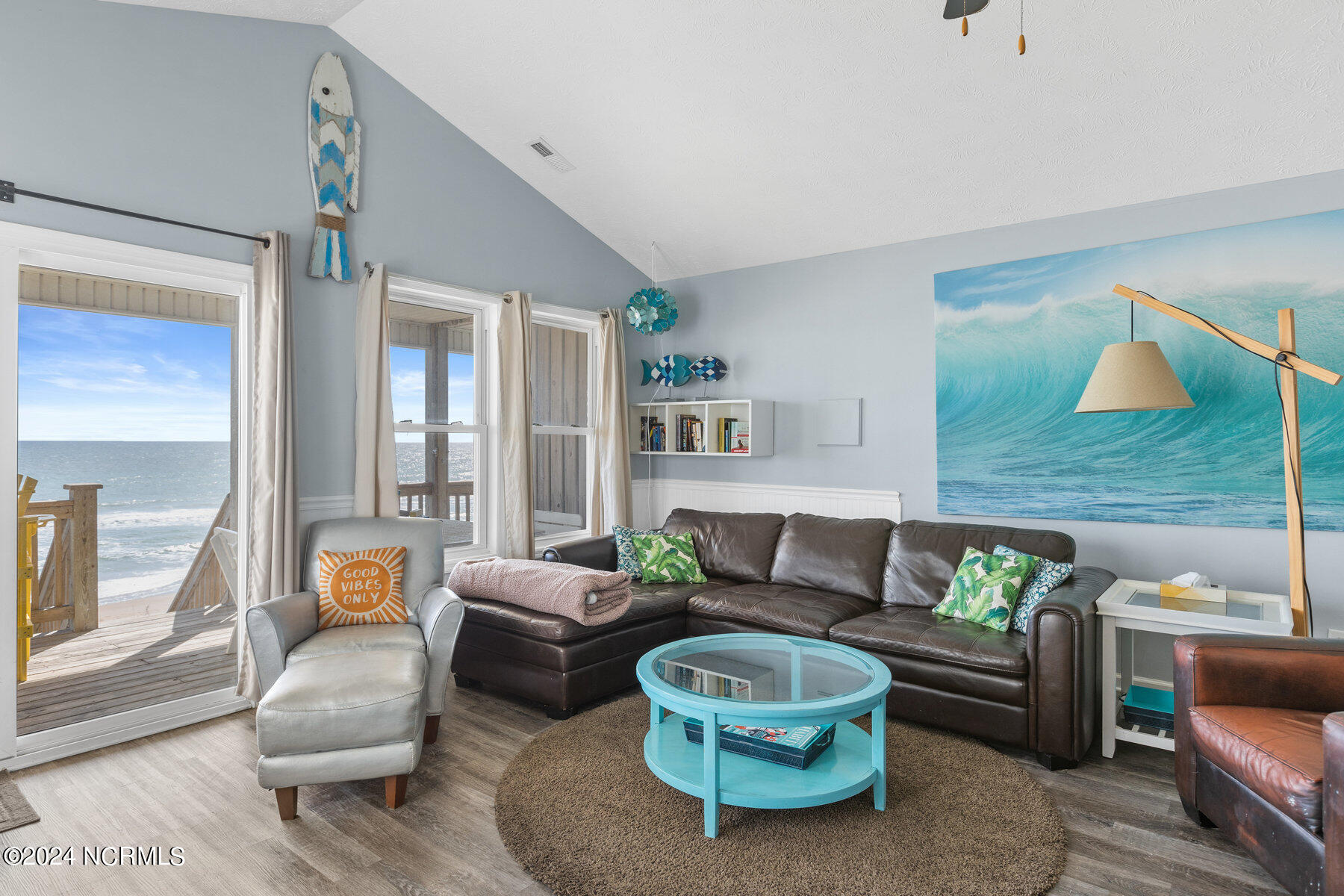 Oceanfront living room with leather sectional, turquoise coffee table, and sliding doors to a deck.