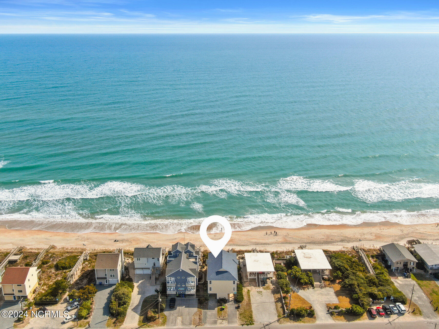 Aerial view of beachfront homes, with a location marker over a house beside the ocean.
