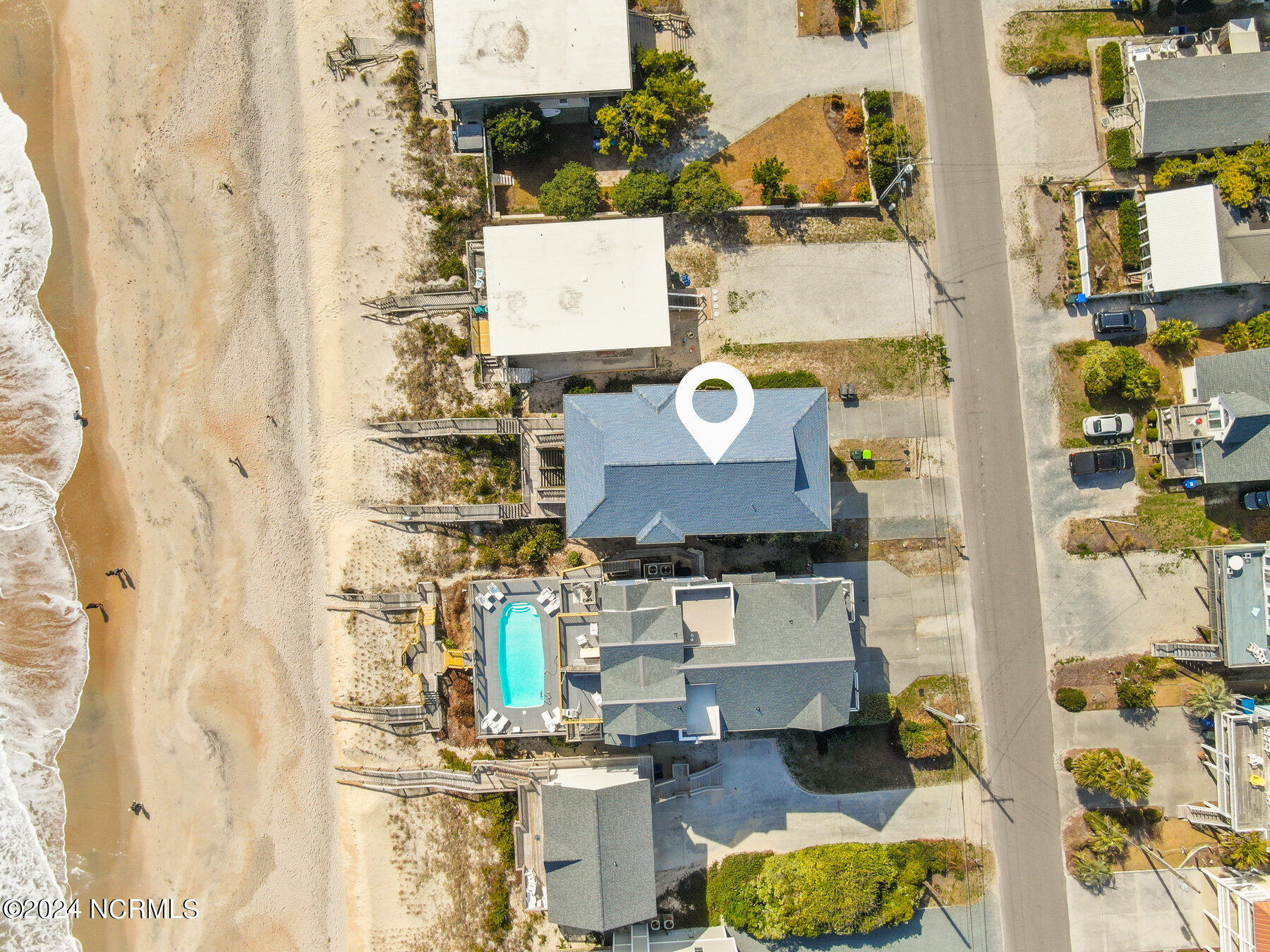 Aerial view of a beachfront home beside the shoreline, marked with a location pin.