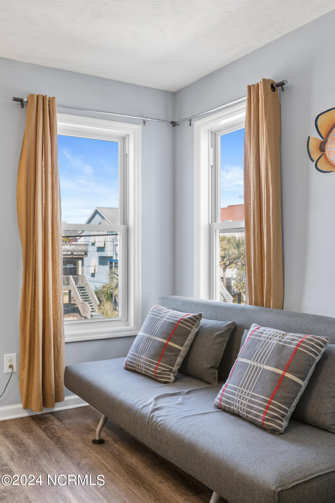 Living room with a gray sofa, plaid pillows, and tall windows overlooking neighboring homes.