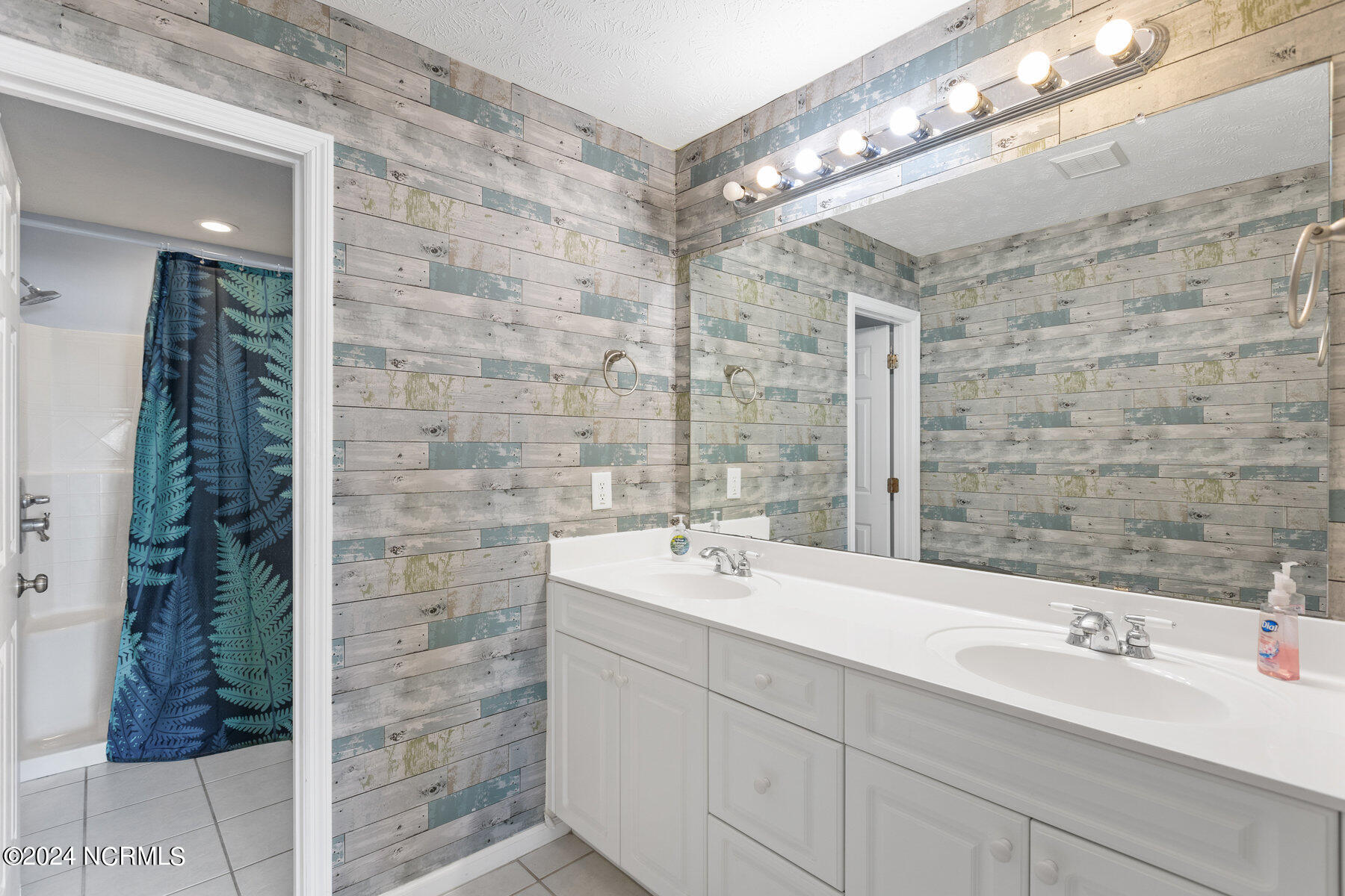 Bathroom with a double-sink vanity, illuminated mirror, and weathered plank walls.