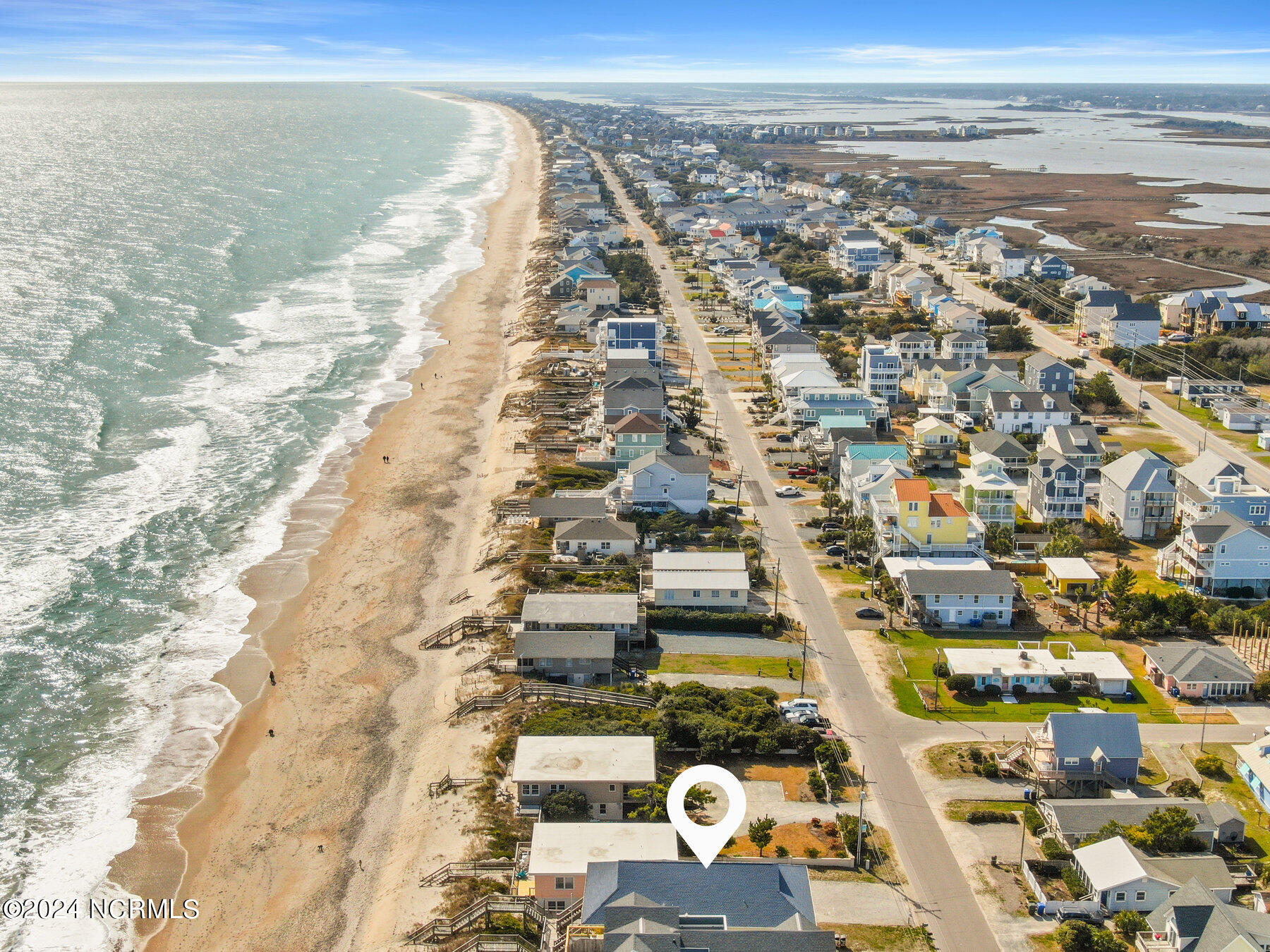 Aerial view of beachfront homes in Surf City, with a white map pin marking a property.