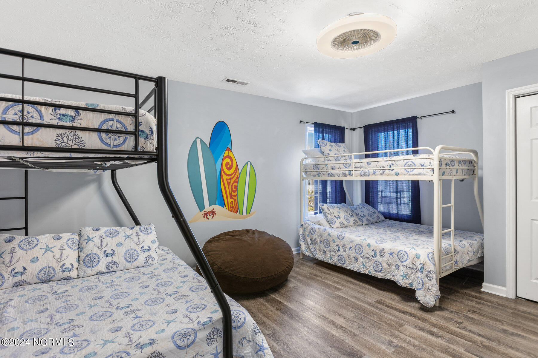 Bedroom with two bunk beds, nautical bedding, surfboard wall art, and blue curtains.