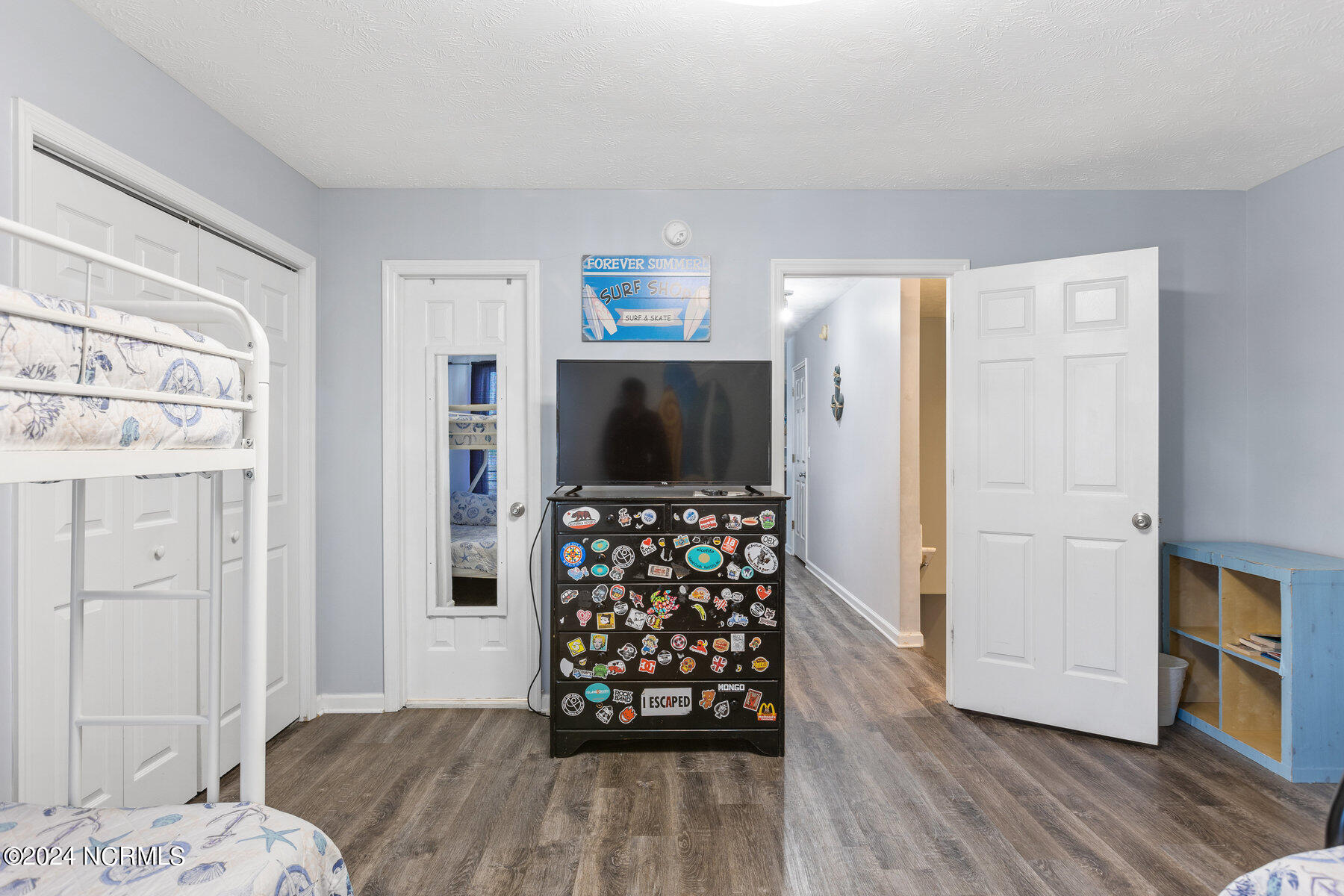 Bedroom with white bunk beds, a sticker-covered dresser, and surf-themed decor.